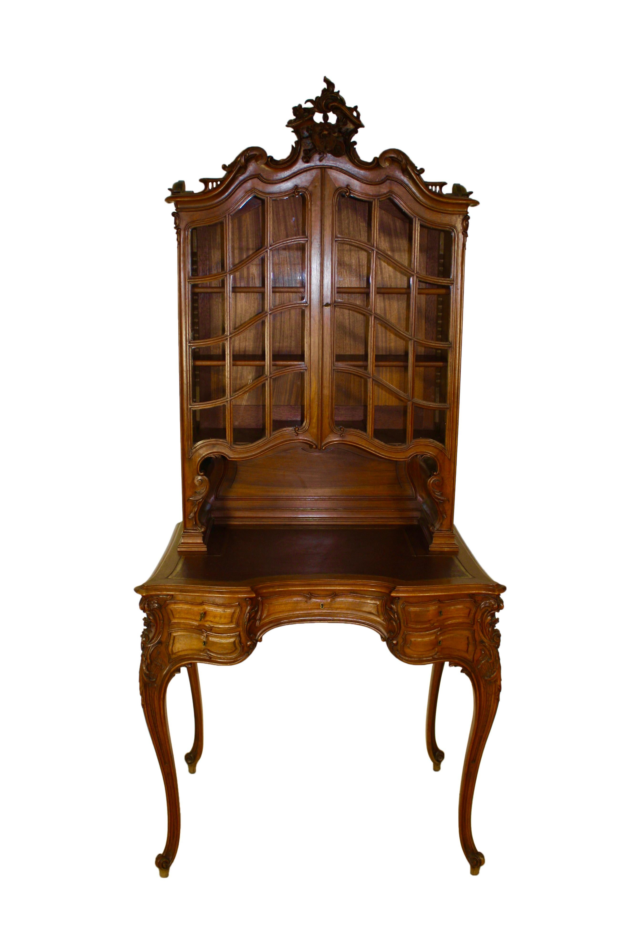 Manufactured by Mercier Frères of Paris, this elegant walnut desk features extensive, detailed carving; a top hutch with double doors and 12 glass panes in each door, opening to two removable shelves; a leather top writing surface embossed with a