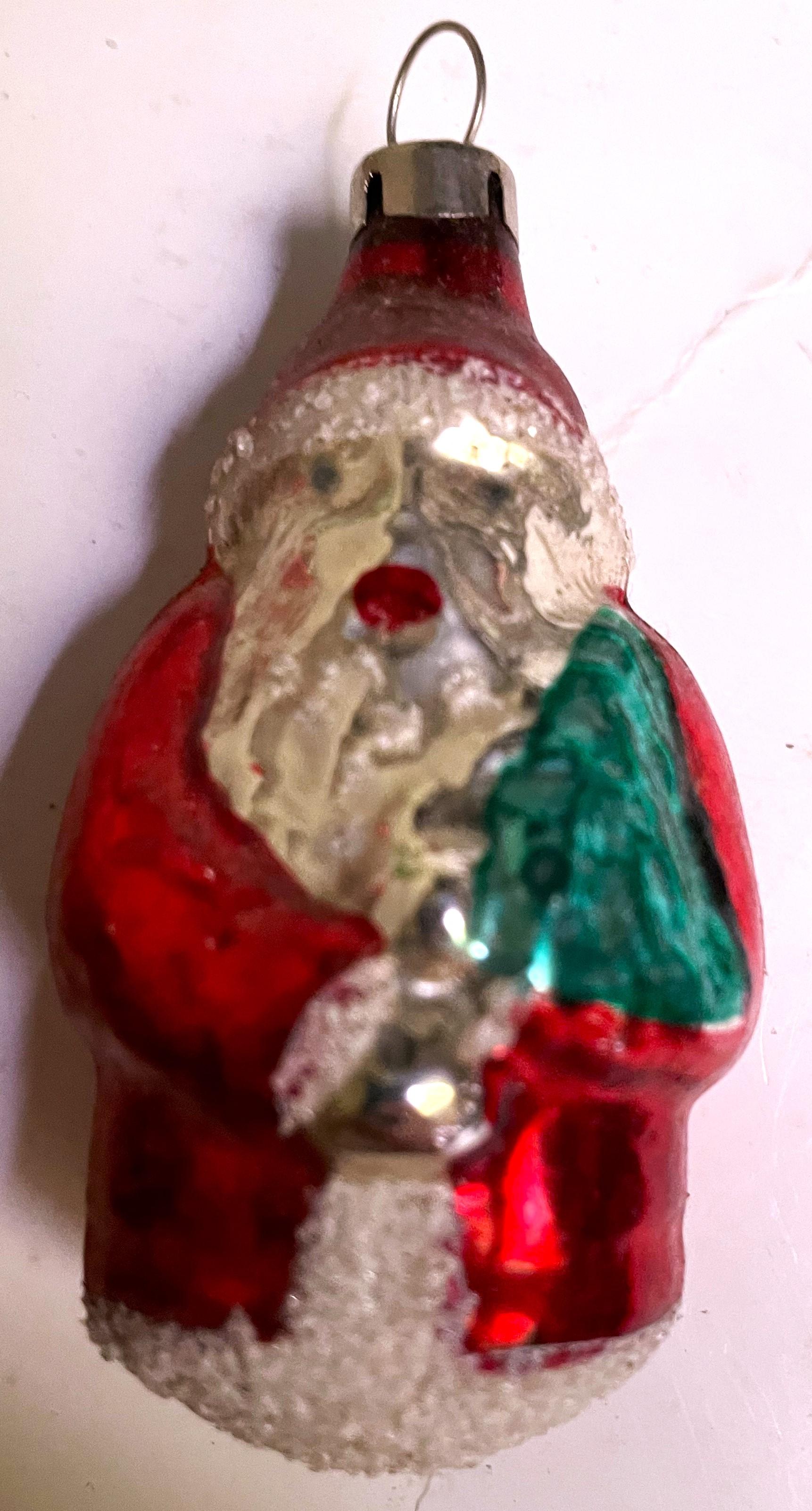 This is an adorable little 














This is an adorable little Santa holding tight to his miniature Christmas Tree. He is bright shiny red on his coat and hat but the red darkens due to age discoloration at the top of the hat where the hook