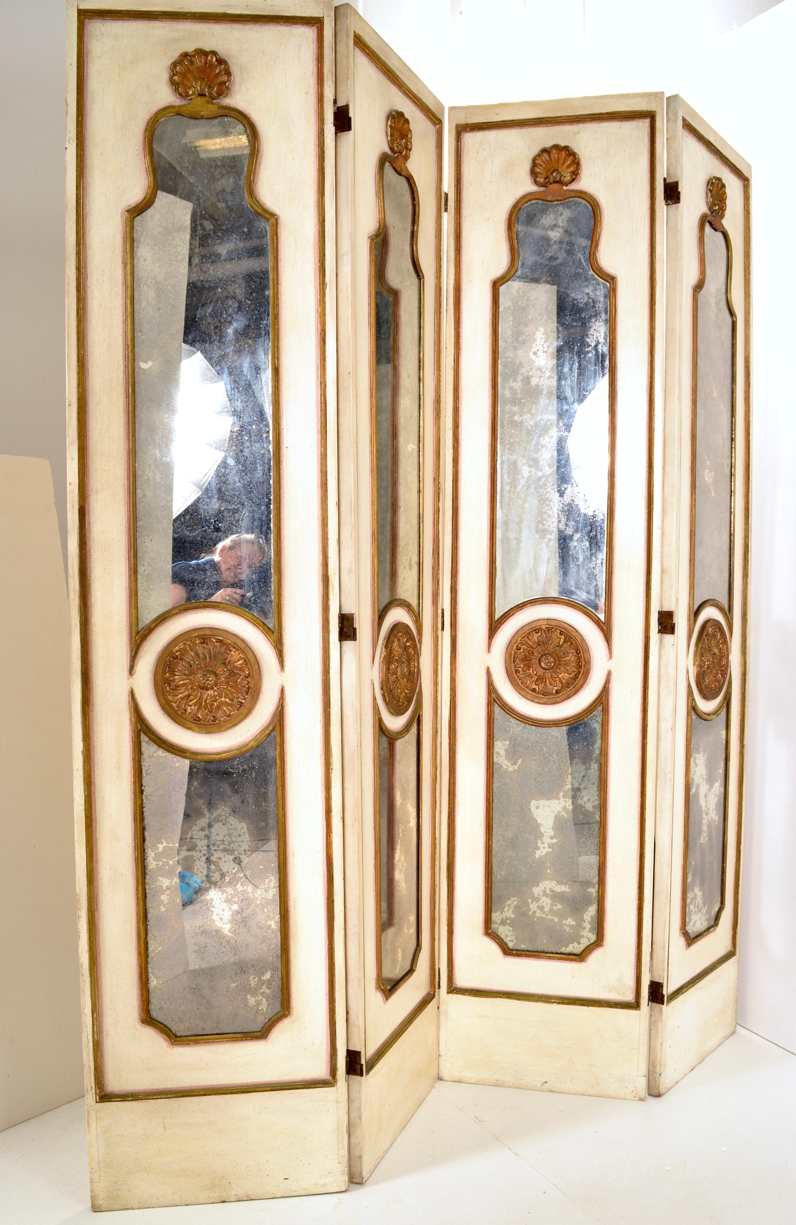 An outstanding example of a Hollywood Regency style. This four panel screen  features four wood panels with hand carved detail surrounding heavily antiqued mercury mirror panels and a central carved and gold painted cartouche. In generally good