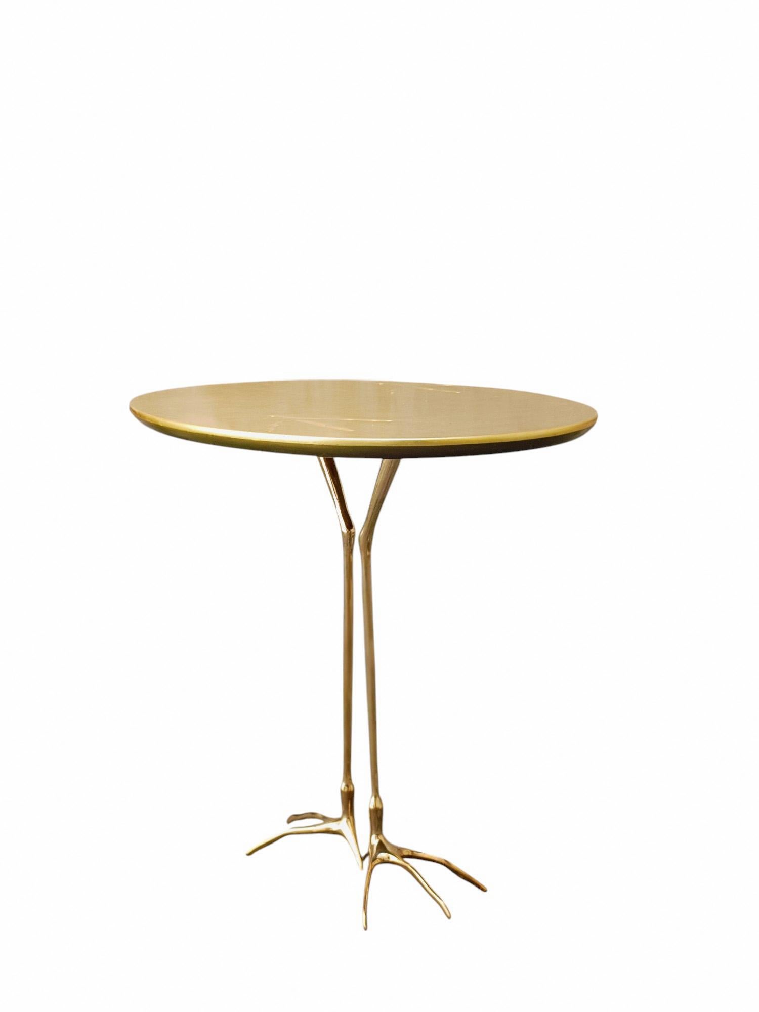 Questo tavolo raro e iconico presenta un piano in legno rivestito in foglia d'oro con tracce di uccelli in rilievo sulla superficie. Poggia su due scultoree gambe in ottone massiccio, a forma di zampe di uccello.Il tavolo originale fu esposto