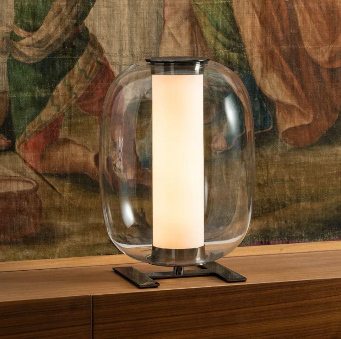 The Meridiano Table Lamp features a unique geometric form with a rounded diffuser made of satin-finish glass. This gently diffuses light, creating a soft, ambient glow perfect for contemporary interiors. The lamp's base is often crafted from