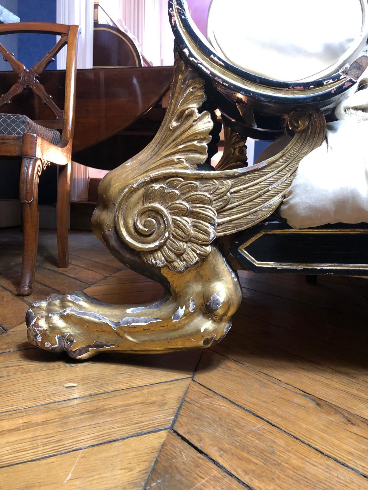 Méridienne à dossier renversé et repose pied en bois mouluré, sculpté, noirci et doré reposant sur quatre pieds griffe. 
Couverture de tissu blanc. 