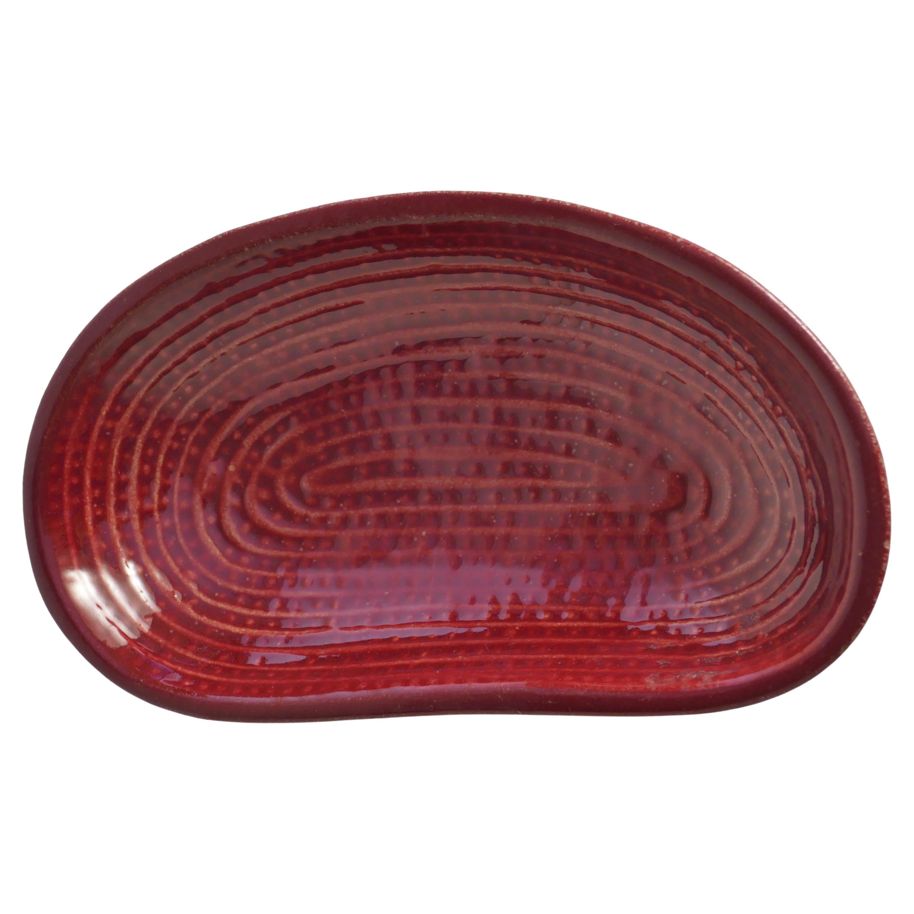 This beautifully hand-crafted Scandinavian modern merlot red stoneware decorative bowl by Andersson & Johansson, Höganäs, features an organic shape with a flat outer surface. Inside, intricate lines spiral inward in smaller circles, while the spaces