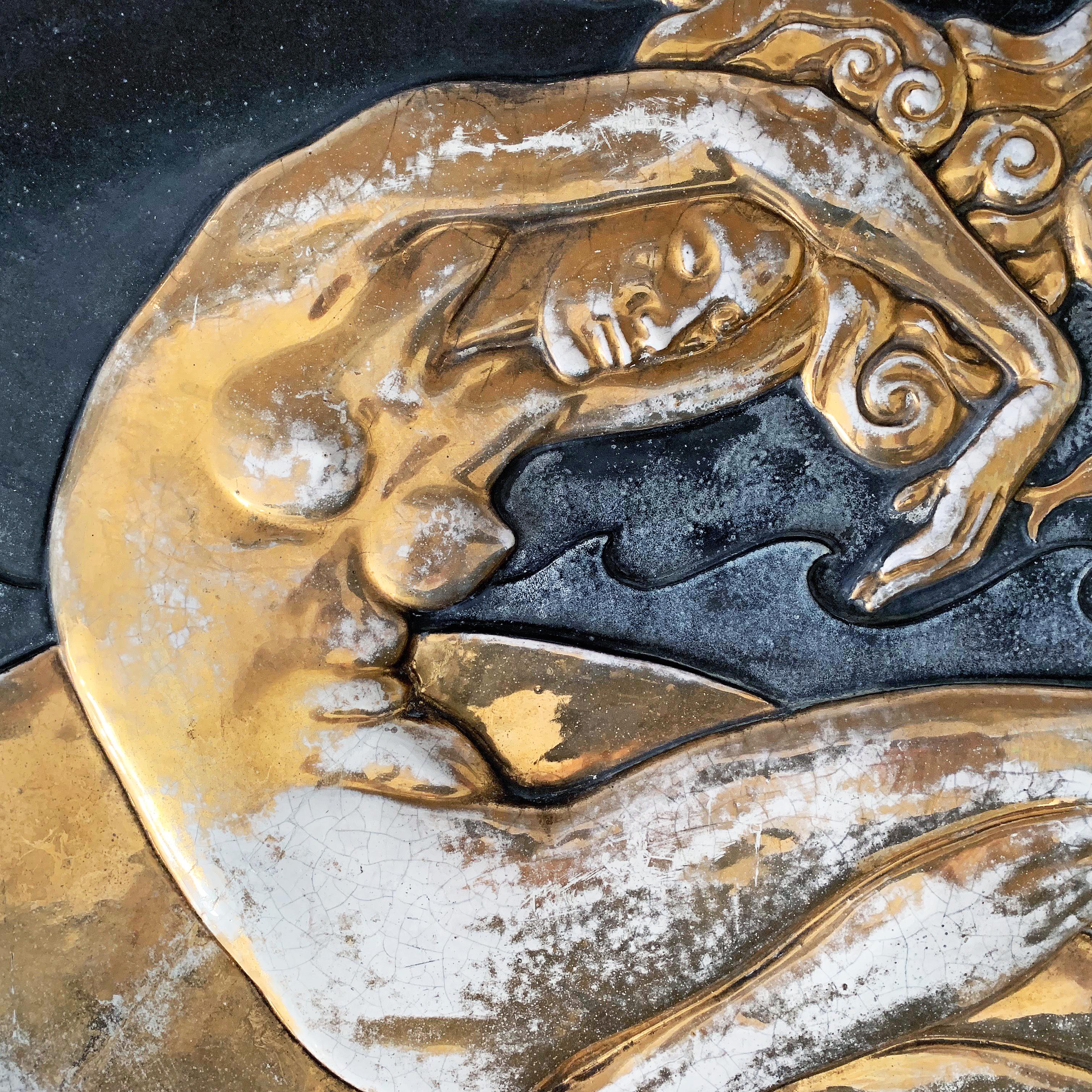 Spectacular in conception and execution, this large bas relief panel in glazed terra cotta depicts a nude mermaid in the foreground, with Art Deco waves and a dolphin in the distance, all finished in gold lustre and deep black glazes. The panel was