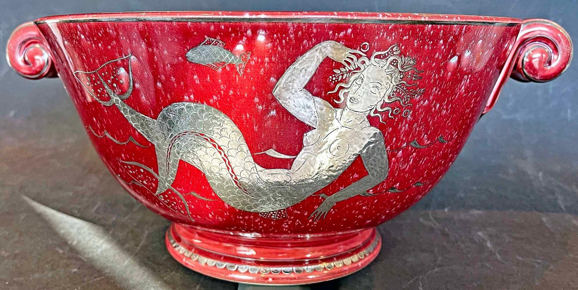 Rare and richly finished in a deep red glaze with tooled silver overlay, this exceedingly rare bowl produced by the Gustavsberg porcelain works in Sweden features a mermaid and fish on its side, and a starfish circumnavigated by circles of stylized