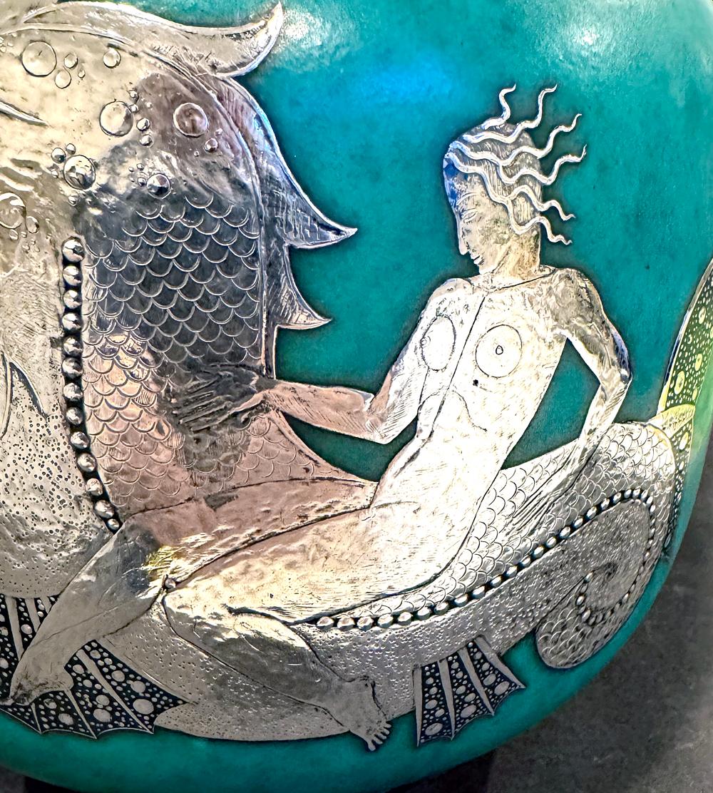 Questo grande e imponente vaso della manifattura svedese Gustavsberg è raro per due motivi: in primo luogo, il dettaglio della sovrapposizione d'argento, che mostra una sirena nuda che cavalca un feroce drago marino, è particolarmente fine; in