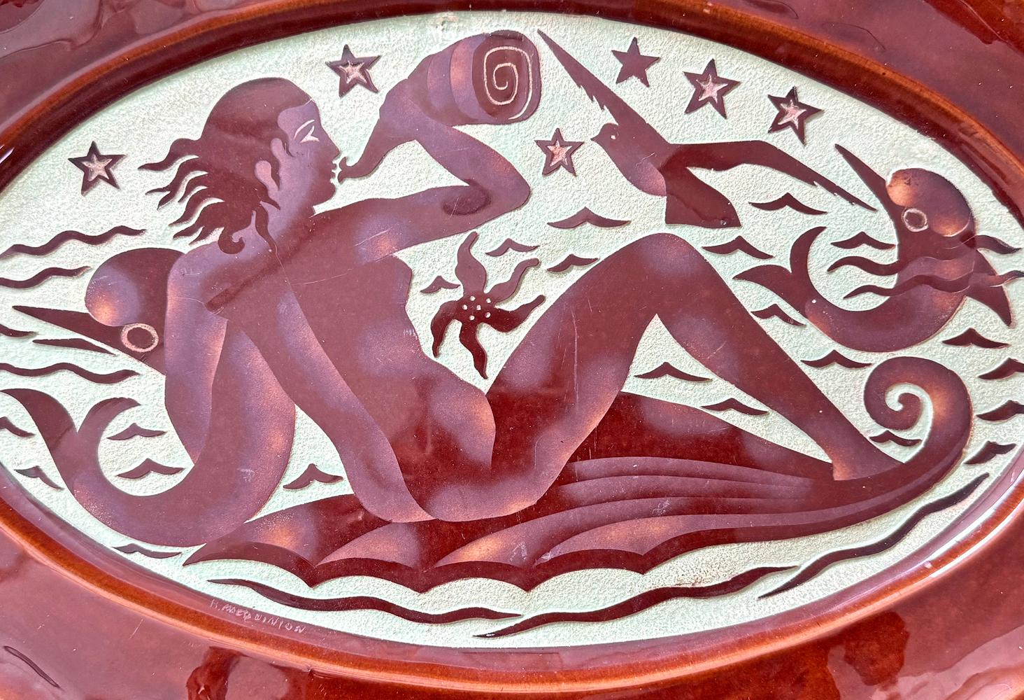 Dieser große und kühne Art-Déco-Keramikteller mit einer Meerjungfrau, die eine Muschel trompetet und einen Delfin umarmt, während sich in der Nähe ein weiterer Delfin und ein Seestern im Wasser tummeln, stammt von Roger Mequinion, der eine völlig