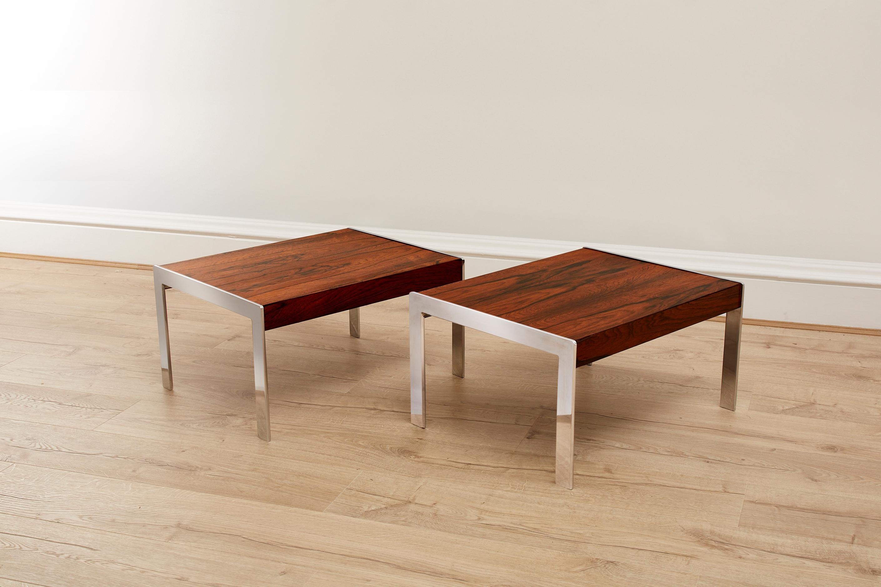An exquisite pair of 1970s Merrow Associates Rosewood and Chrome Side Tables. 

Crafted with meticulous attention to detail, these tables seamlessly blend the warmth of rosewood with the modern appeal of chrome accents. 

Designed by Richard Young