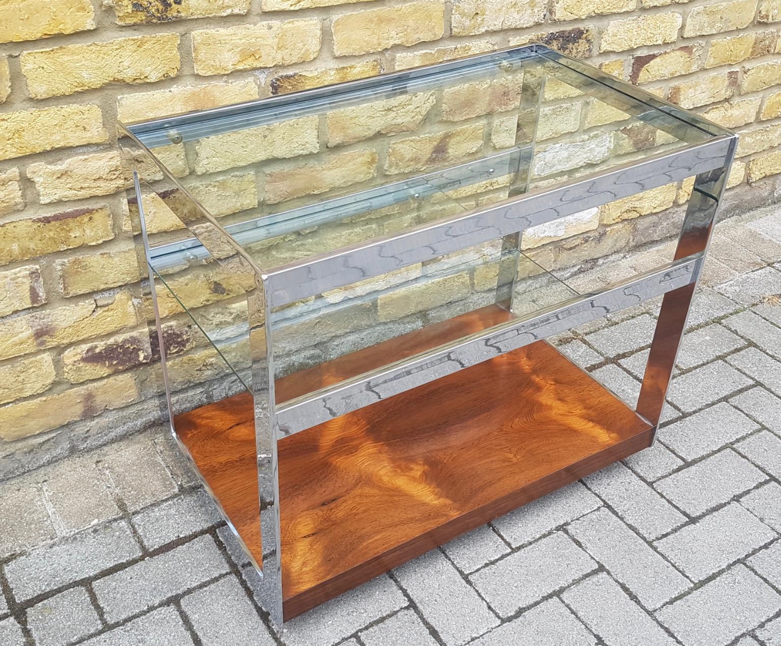 A beautiful and top quality drinks trolley by Merrow Associates, this dates from the 1960s-1970s. It has a very well made chrome frame, thick glass shelves and a stunning rosewood base. The condition is superb for its age, there are just a few minor