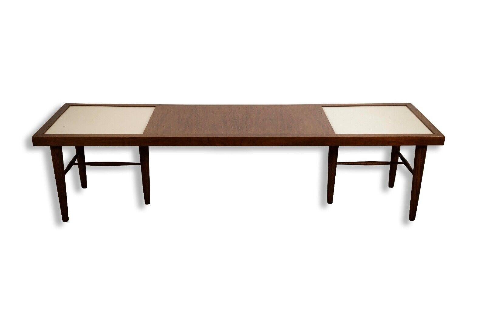 The Merton Gershun for American of Martinsville Coffee Table in Walnut is a quintessential piece of mid-century modern design. Crafted with the finest walnut wood, this coffee table exudes timeless elegance and sophistication. Its sleek lines,