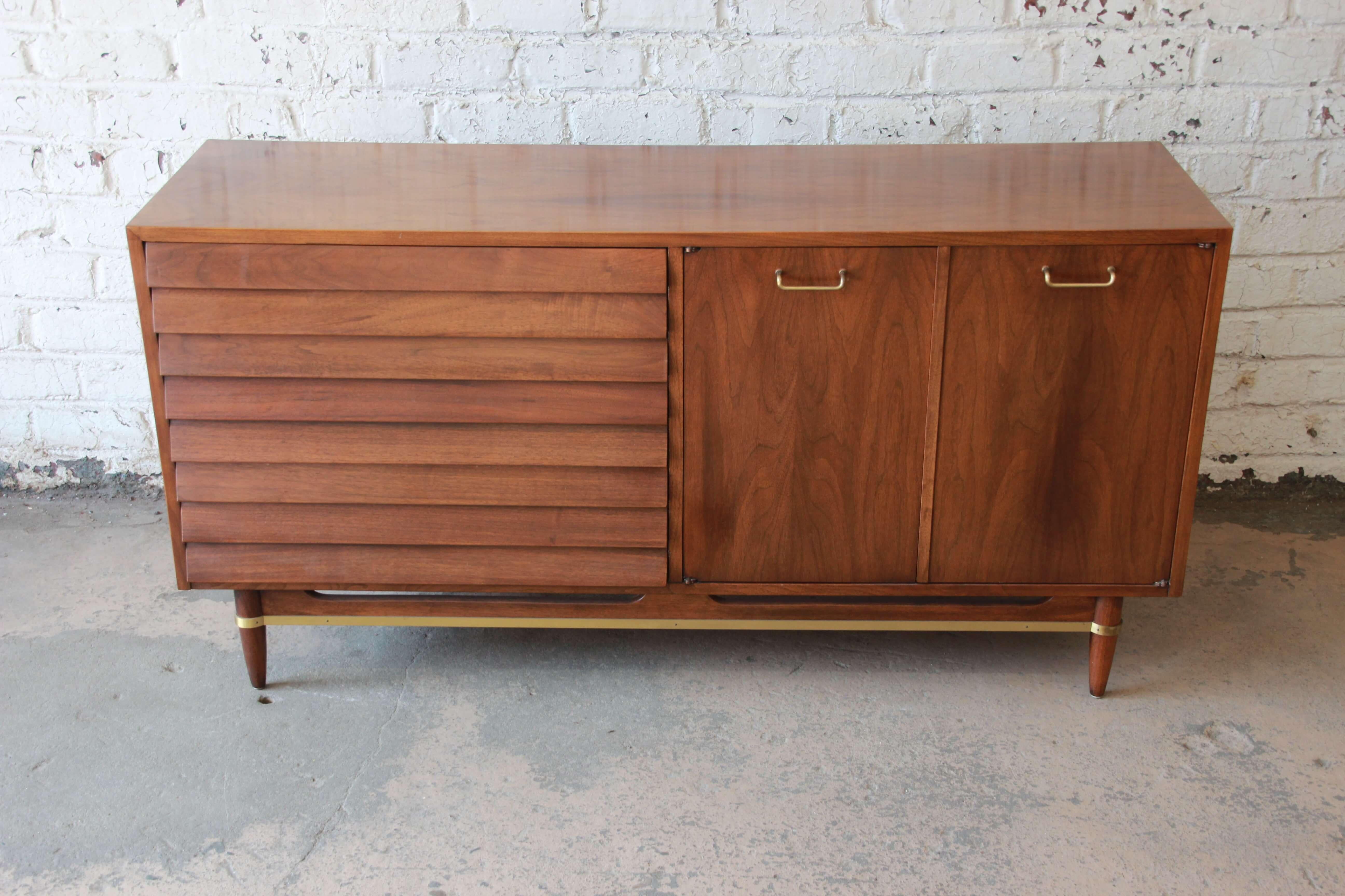 Offering an excellent original condition Merton Gershun for American of Martinsville dresser or credenza. This popular design has louvered drawers, brass pulls, and brass trim. The right cabinet doors open to reveal three drawers and a cabinet area.