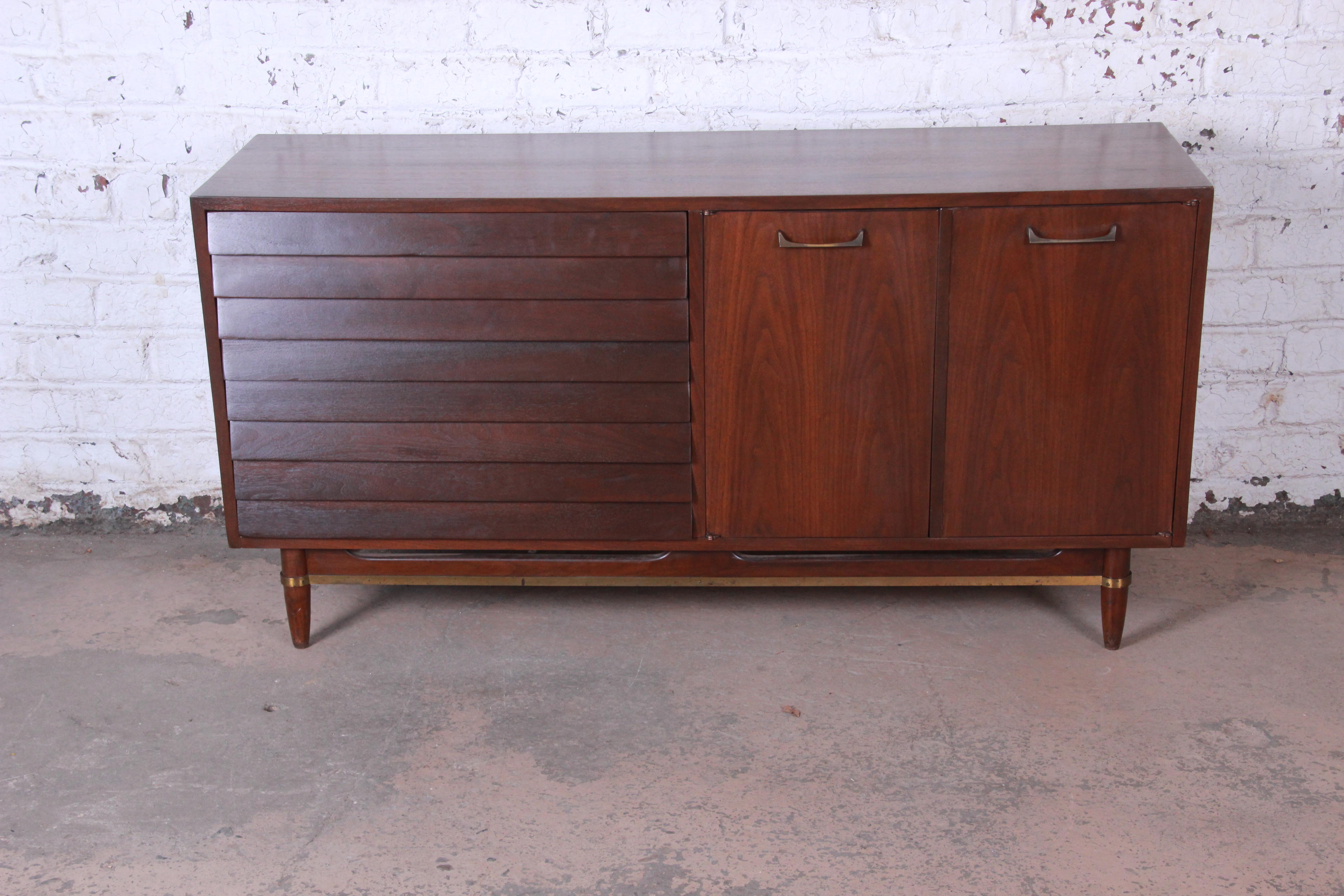 A nice Mid-Century Modern louvered front sideboard credenza by Merton Gershun for American of Martinsville. This popular design has louvered drawers, brass pulls, and brass trim. The right cabinet doors open to reveal three drawers and a cabinet