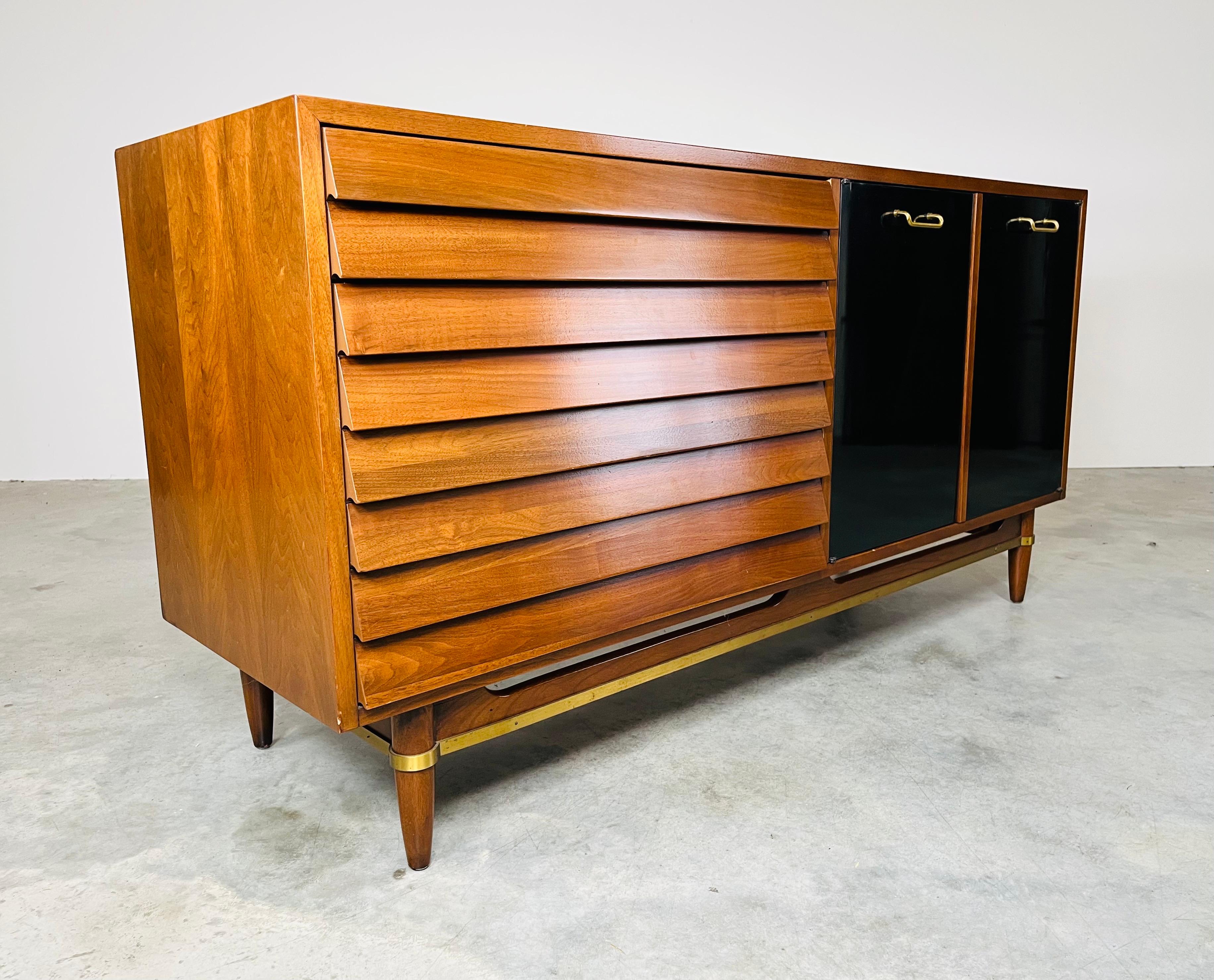 An attractive multi-functional lowboy credenza having high-gloss black lacquer doors with solid brass pulls covering center single shelf storage and 3 cream colored deep drawers. To the left are 3 storage drawers faced with carved walnut angled
