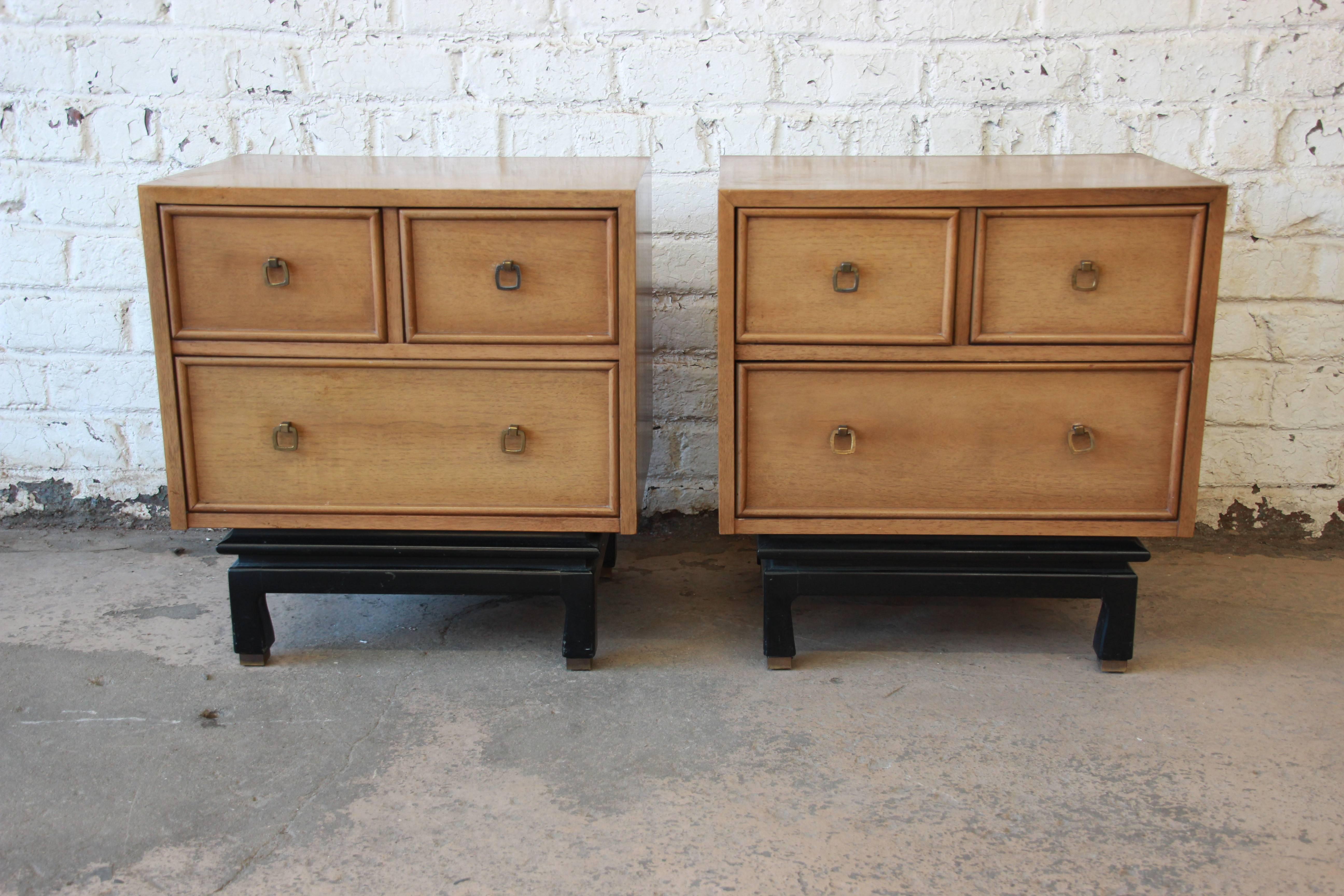 A stylish pair of Mid-Century Modern Asian inspired nightstands or end tables designed by Merton Gershun for American of Martinsville. The nightstands feature beautiful bleached walnut wood grain and original brass drawer pulls. They are accented