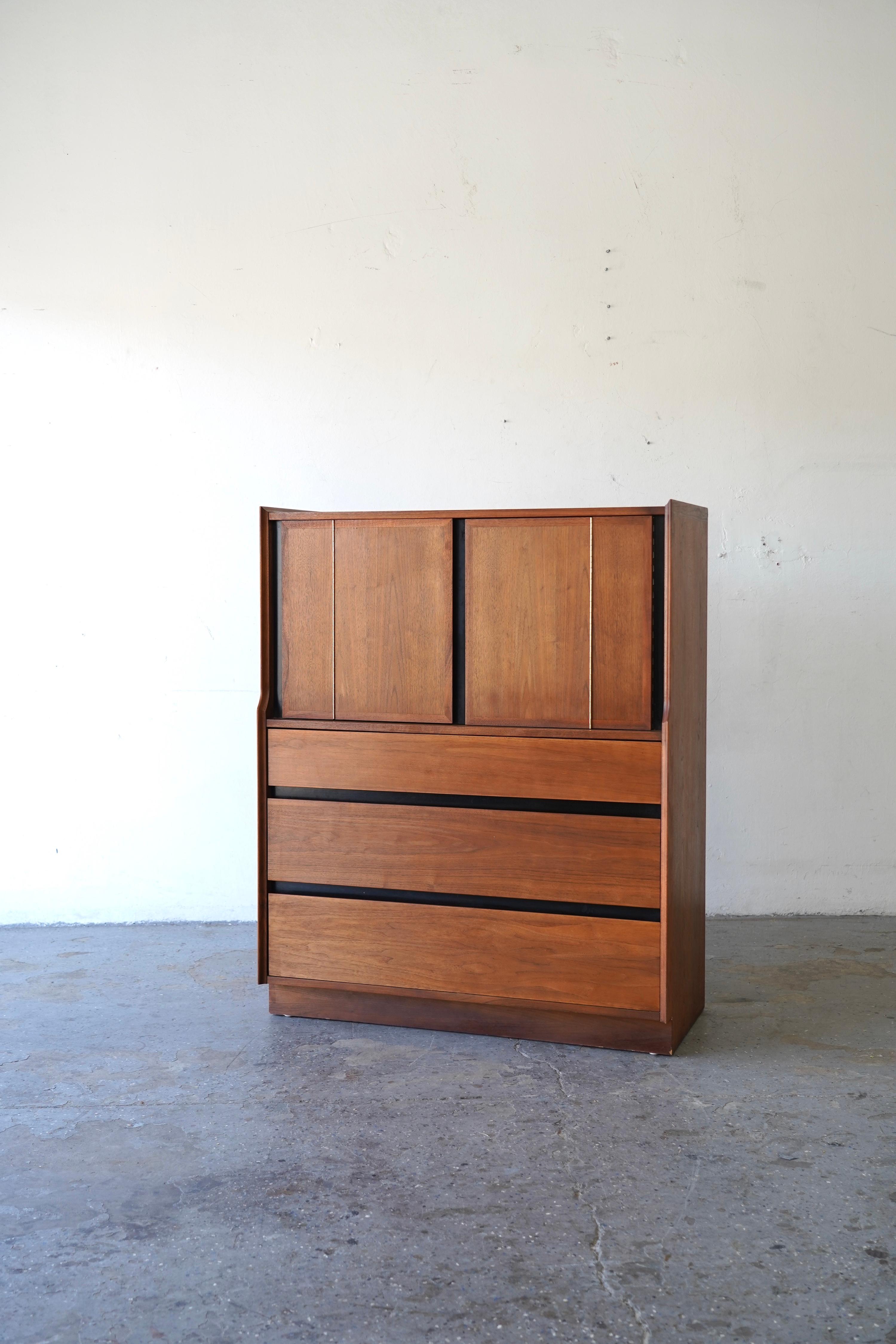 Una cassapanca da uomo in noce, moderna e pulita, perfetta per essere utilizzata come mobile contenitore in camera da letto o come elegante mobile bar. La sezione superiore presenta una coppia di ante a pannello che si aprono per rivelare uno