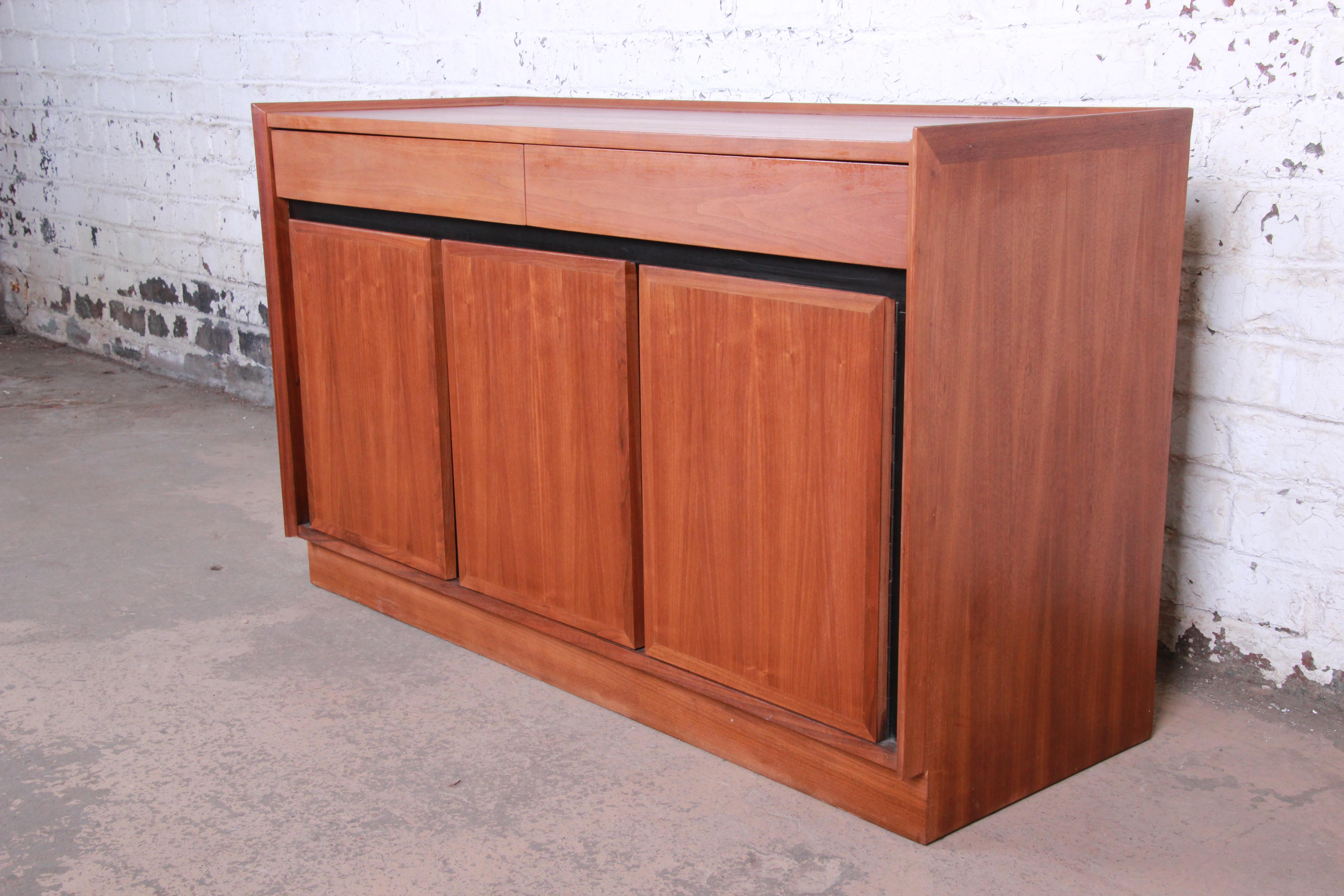 A gorgeous Mid-Century Modern walnut sideboard or credenza designed by Merton Gershun for Dillingham. The credenza features beautiful walnut wood grain with ebonized trim and sleek mid-century design. It offers ample storage, with two long drawers