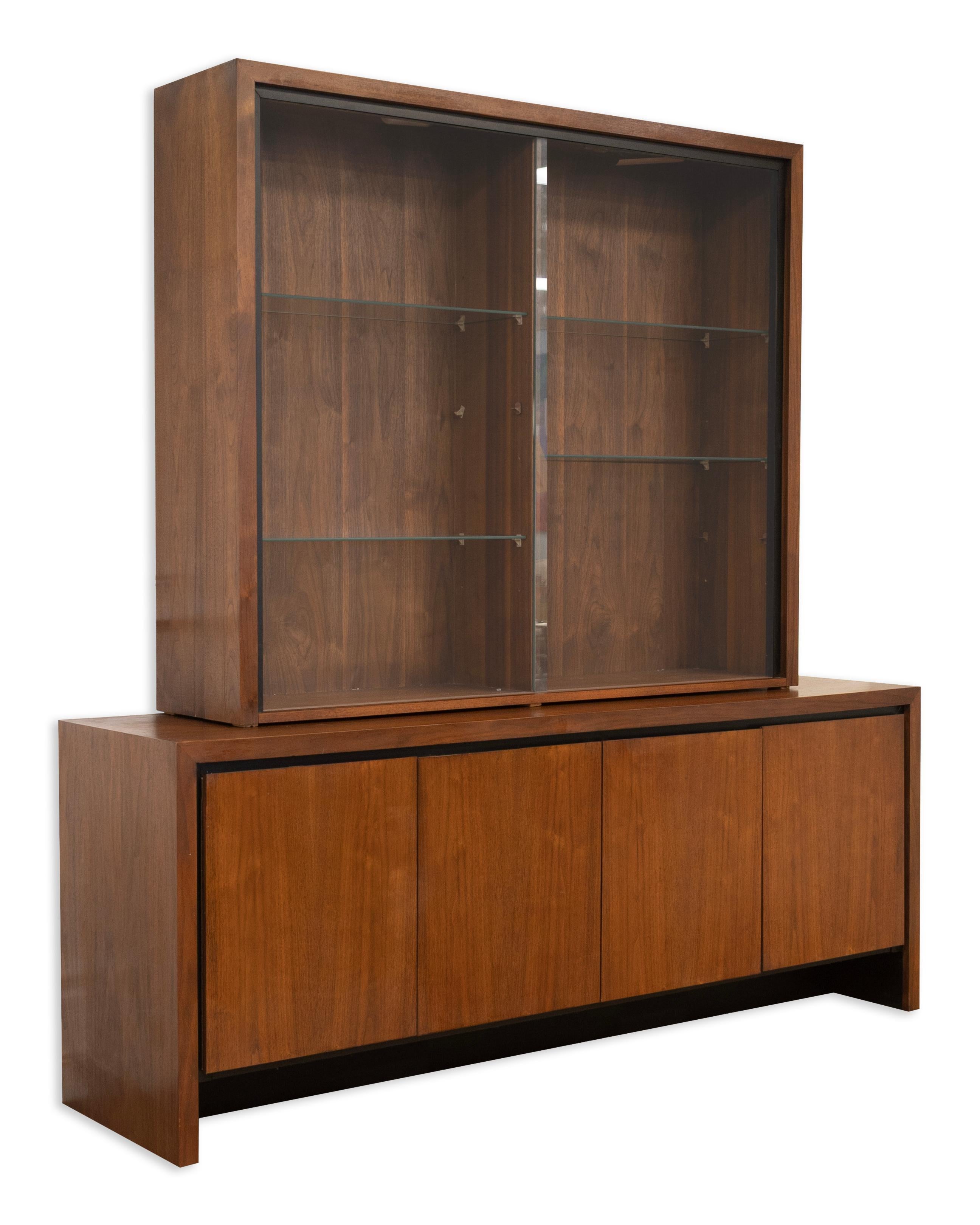 Questo mobile per le porcellane in noce a due pezzi di Merton Gershun per Dillingham esemplifica le linee pulite e l'eleganza funzionale del design di metà secolo. La credenza inferiore è dotata di quattro ante che si aprono per creare ampi spazi,