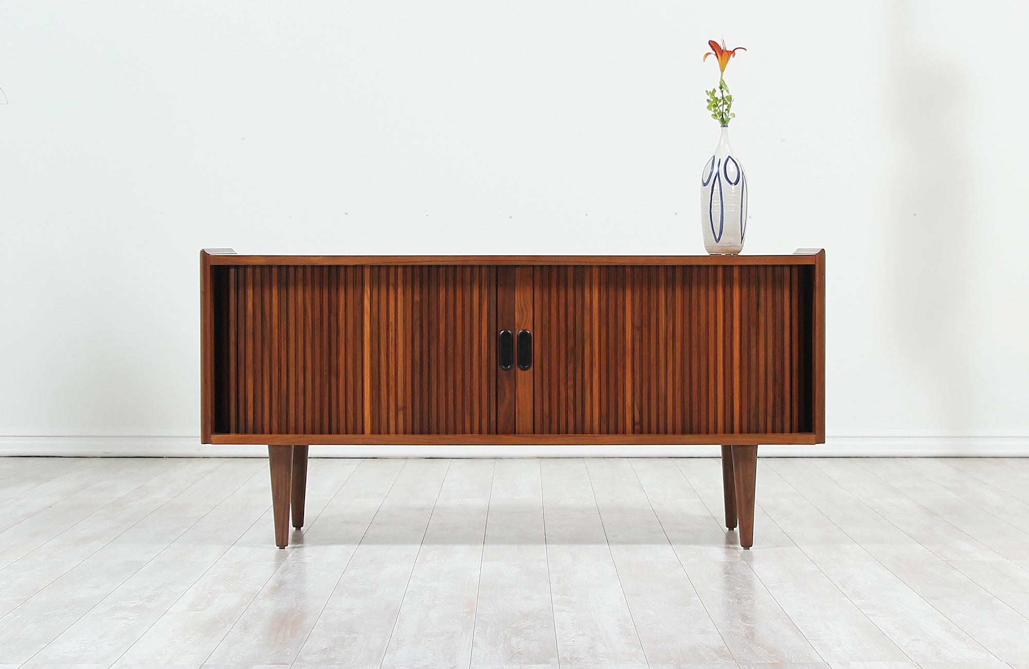 Compact Mid-Century Modern tambour-door credenza designed by Merton L. Gershun for Dillingham in the United States, circa 1960s. Impeccably crafted with walnut wood and newly refinished by our skilled craftsmen, this credenza features two tambour