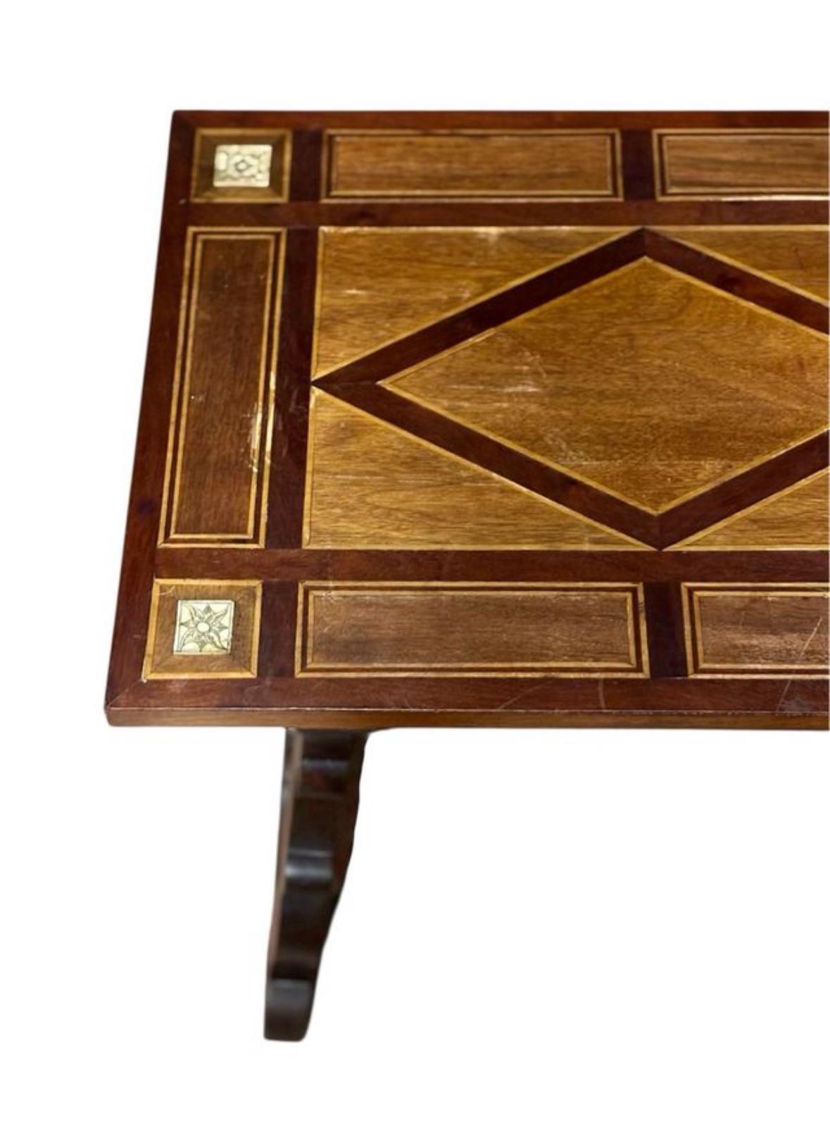 Mesa baja auxiliar Circa 1.940, realizada en madera de nogal, con marquetería en el sobre, patas de lira talladas y crucetas de hierro forjado.
