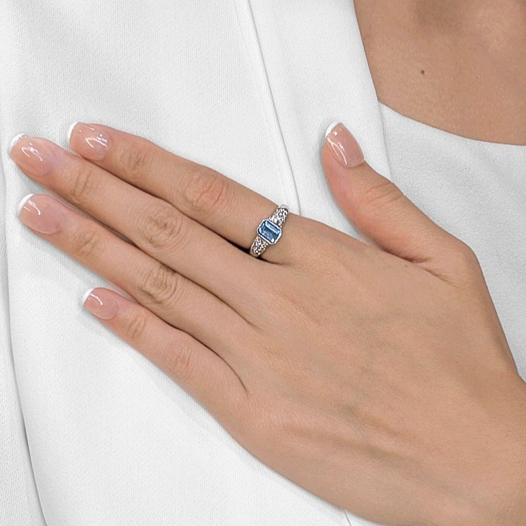 A breath of serenity wrapped in luxury — this refined ring features a 1.00ct emerald-cut aquamarine that radiates tranquil light blue hues. Set in lustrous 18K white gold, the center stone is accented by 18 natural round brilliant diamonds totaling