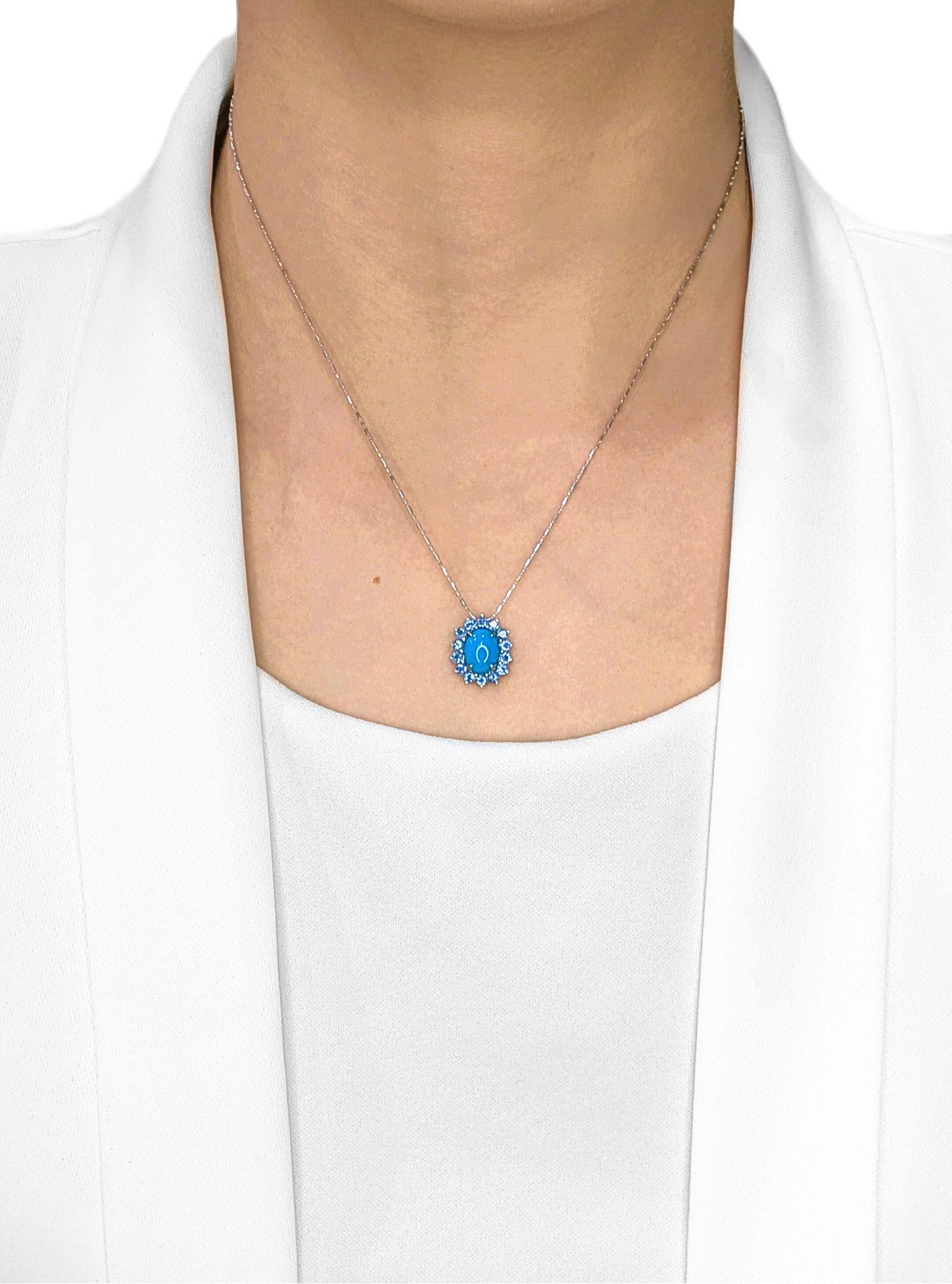 Une touche de couleur avec une touche de luxe - ce pendentif est centré sur une turquoise cabochon lisse de 1,52ct, qui brille dans une teinte bleue vive, à la fois audacieuse et raffinée. Autour d'elle, un halo de 14 saphirs ronds taillés en