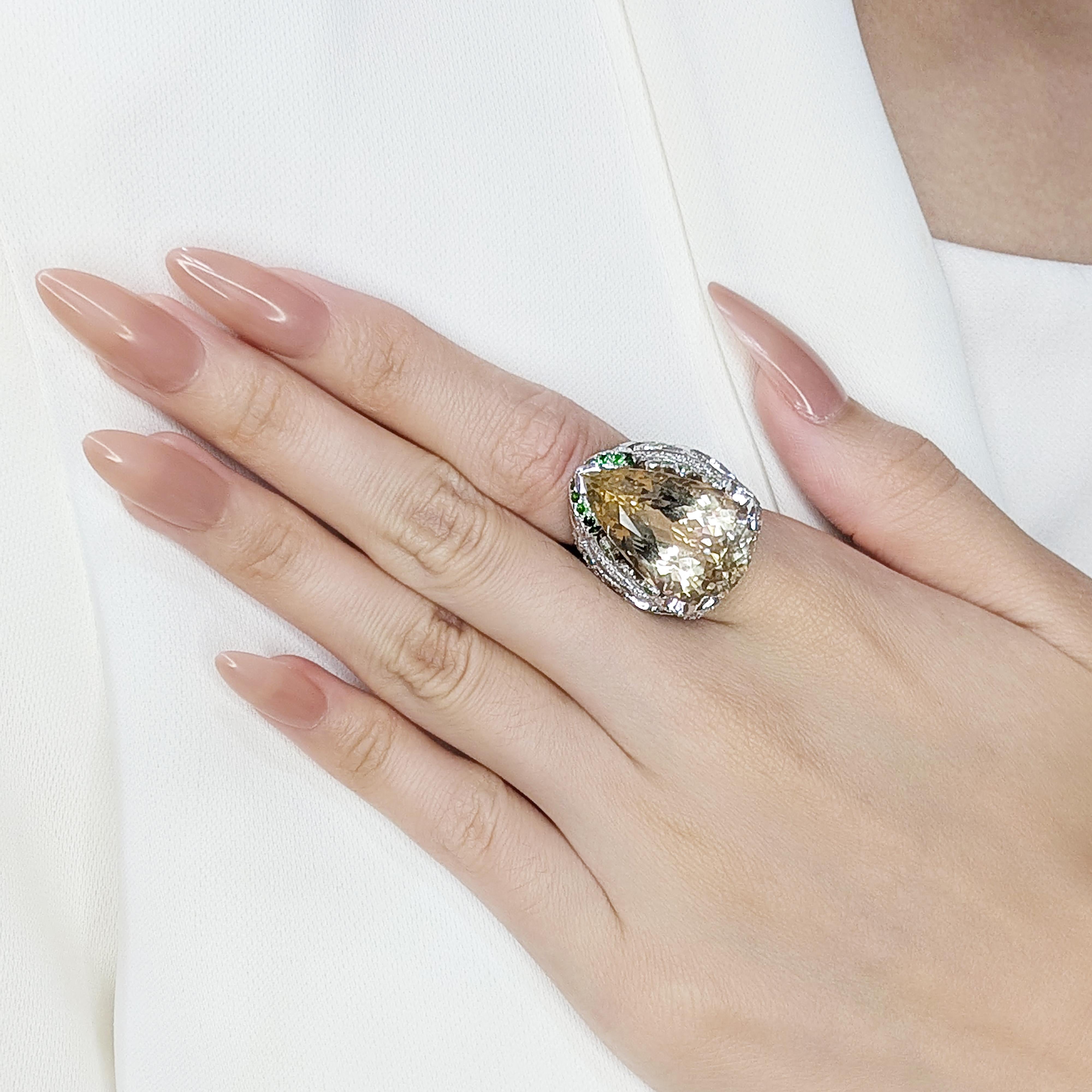 This pre-owned ring is a bold and mesmerizing piece, designed to captivate with its striking combination of gemstones. Crafted in elegant 18K white gold, it features a remarkable 24.04ct pear-shaped citrine as its centerpiece, showcasing a vibrant
