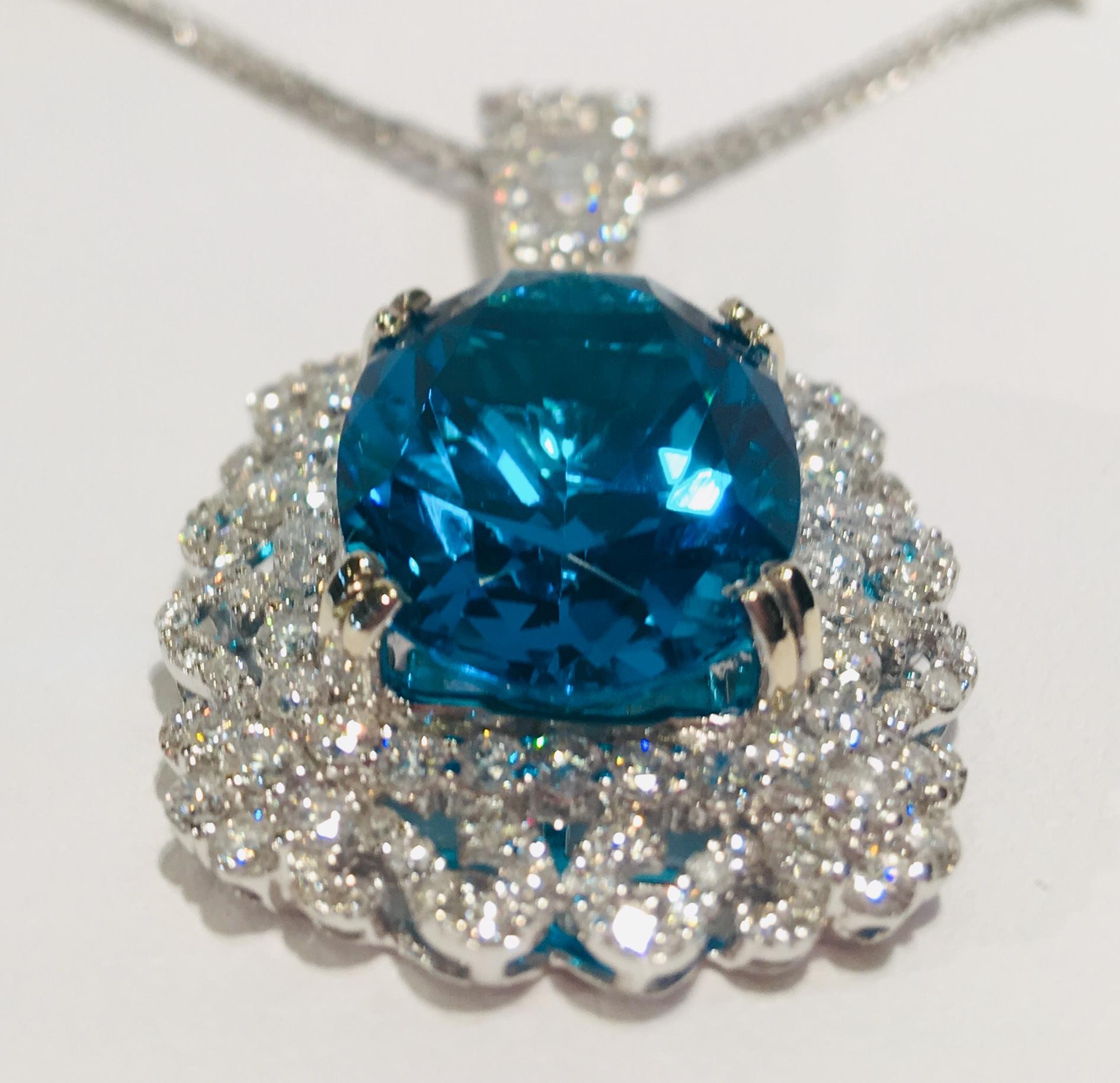 A huge, oval cut, deeply saturated teal color apatite is talon prong set in 18 karat white gold and surrounded by a fantastic halo of round brilliant diamonds set in an openwork, curlicued, floral pattern and accented by a large, tapered diamond