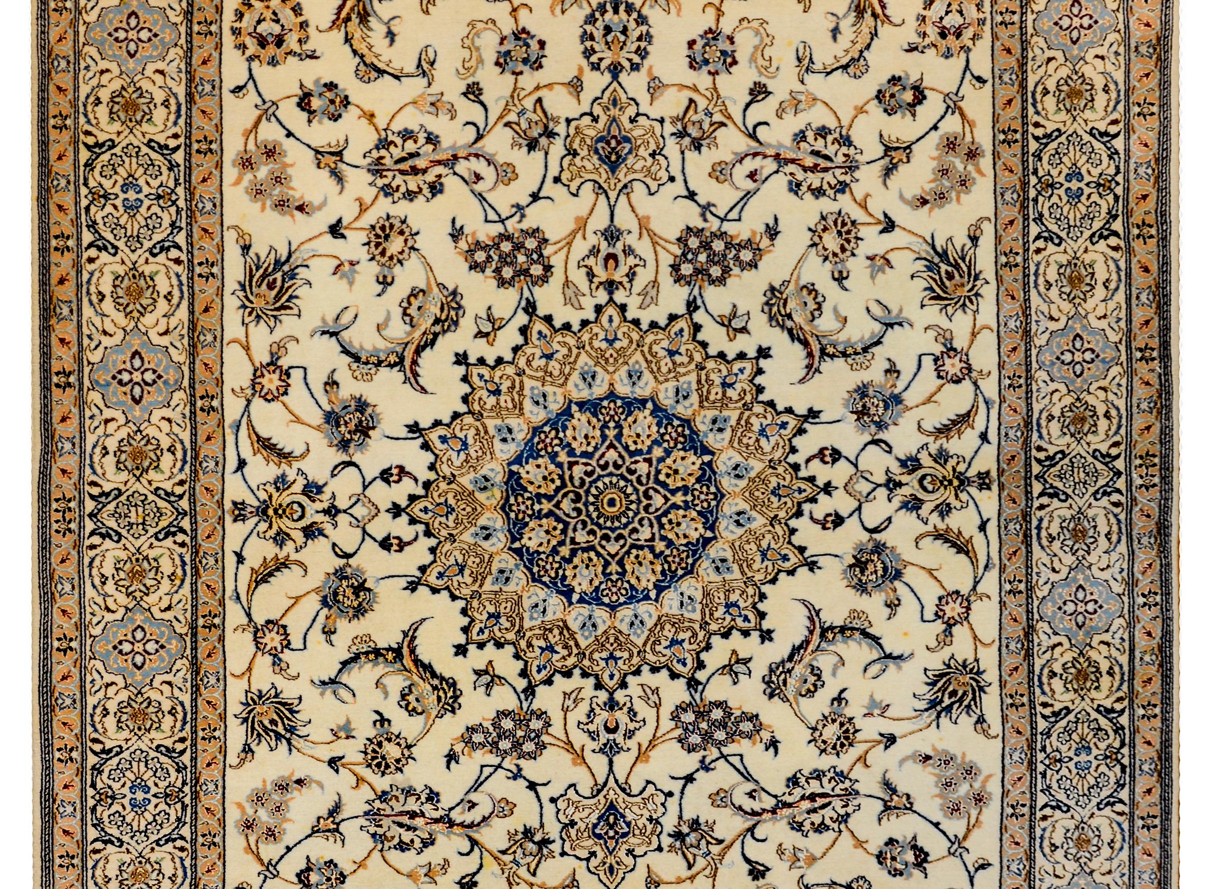 A mesmerizing late 20th century Persian Isfahan silk and wool rug with a large central circular medallion amidst a field of scrolling vines and large flowers and leaves, all woven in light and dark indigo, gold, and brown, on a cream colored ground.