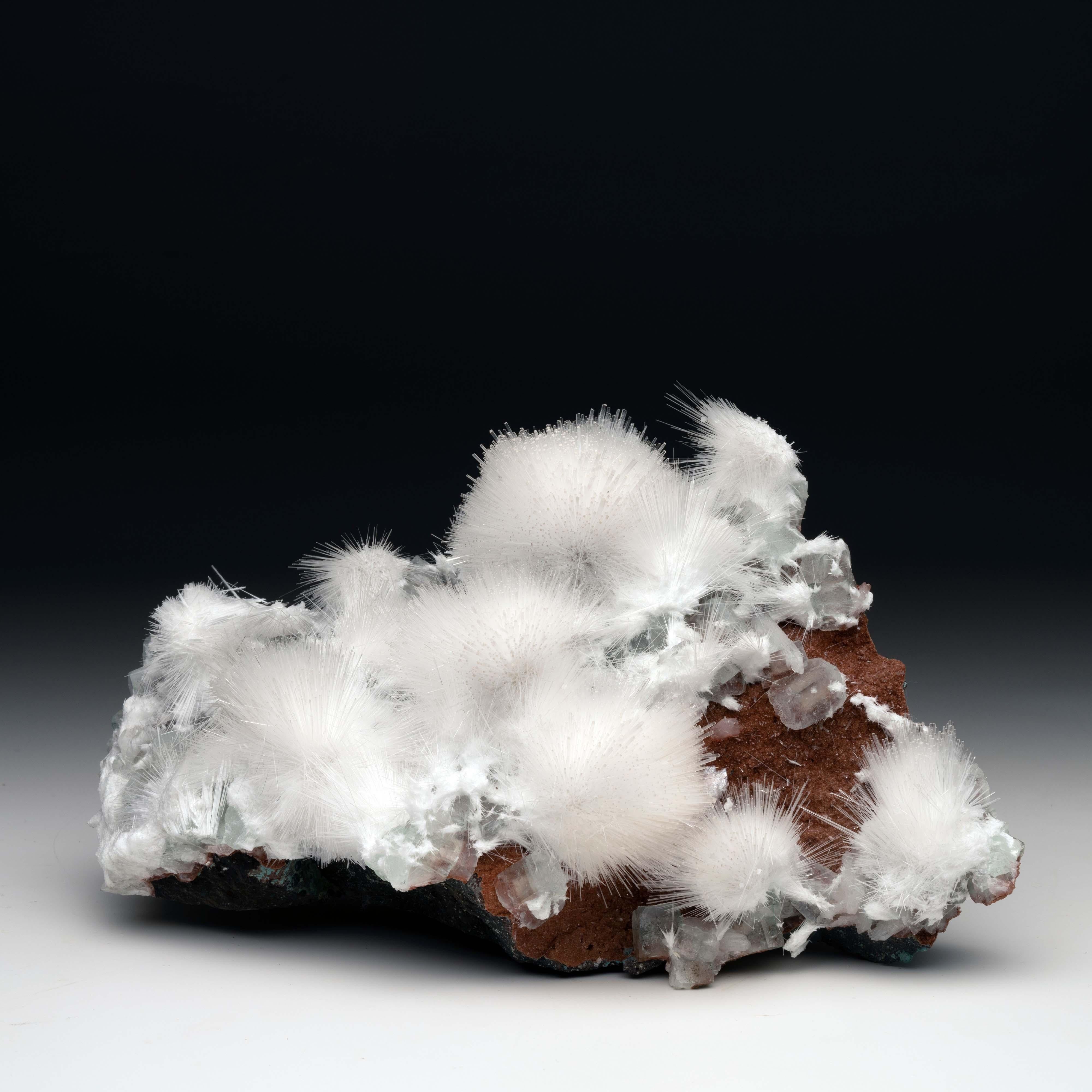This mesolite and apophyllite on a red heulandite matrix was mined out of an extremely small pocket in India. Puffs of white mesolite layer over apophyllite on a rocky bed. The white mesolite and clear apophyllite beautifully contrast the deep red