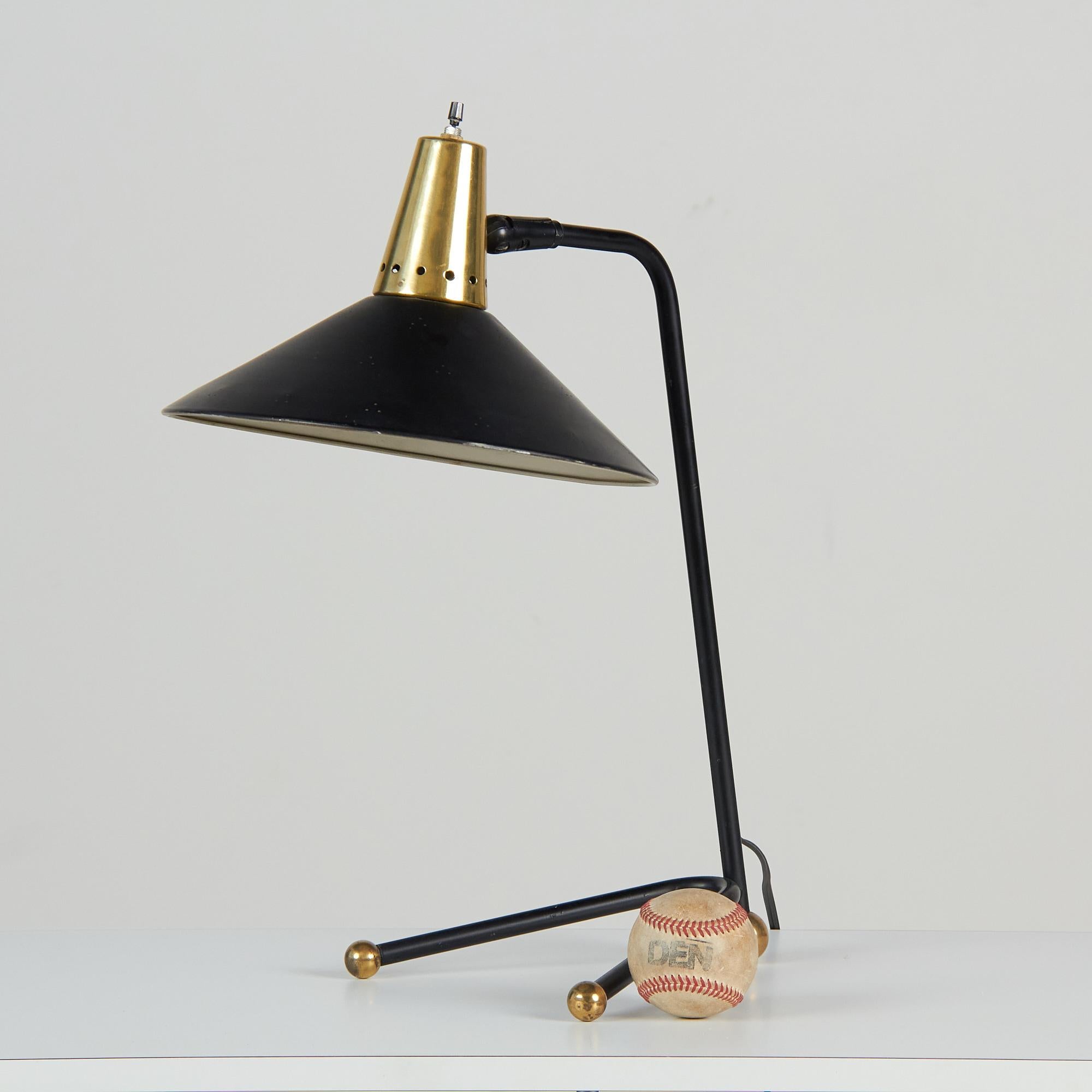 This metal and brass desk lamp, c.1960s, Italy, in the style of Stilnovo, is a beautifully moody accent piece. It features a minimalist enameled black steel body and shade with brass details at the balls of each foot and atop of the articulating
