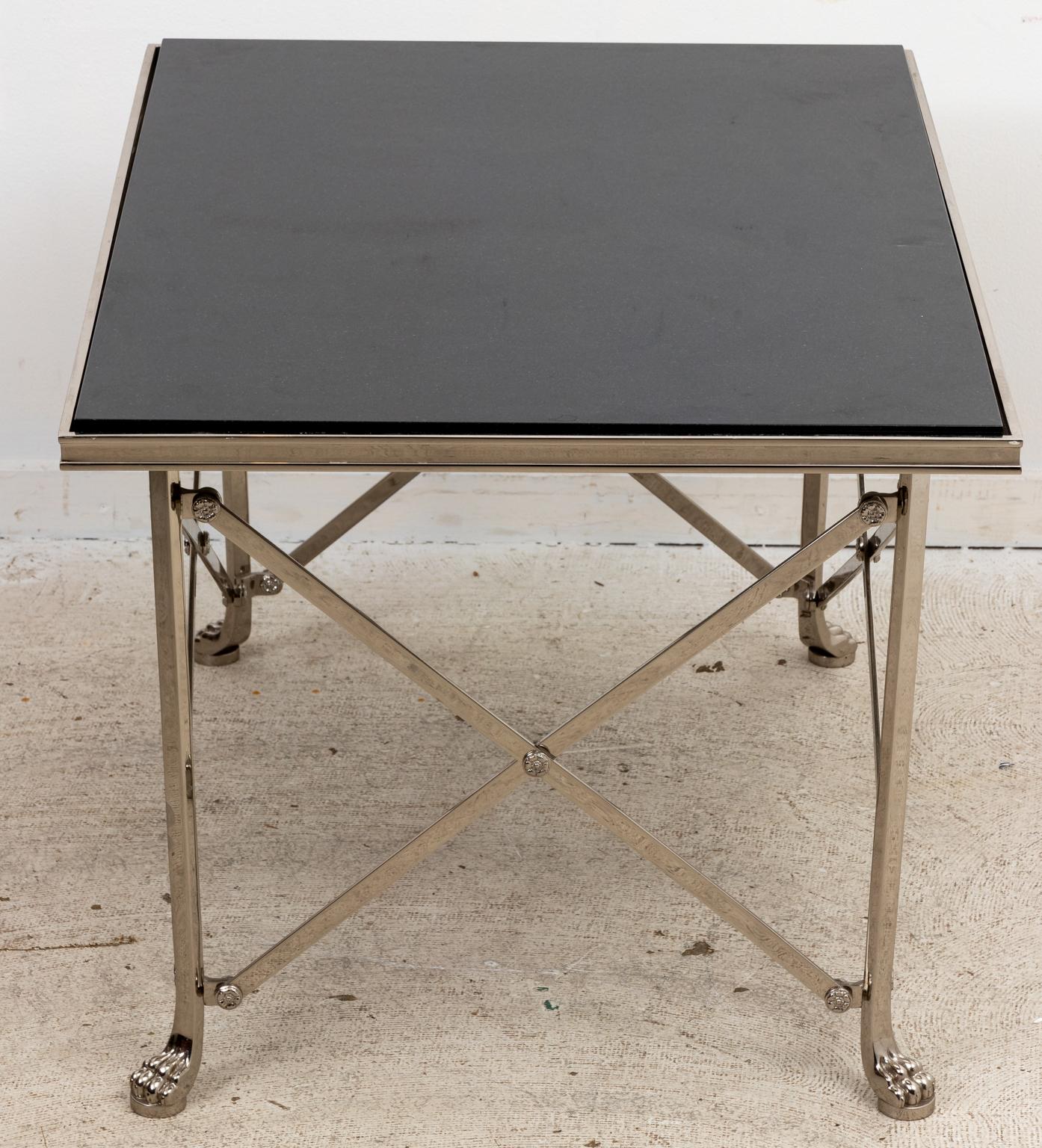 Contemporary granite top tea table on a polished metal x-frame base with lion's paw feet. The table's base is further embellished with rosette medallions. Please note of wear consistent with age including patina to the granite tabletop and metal.