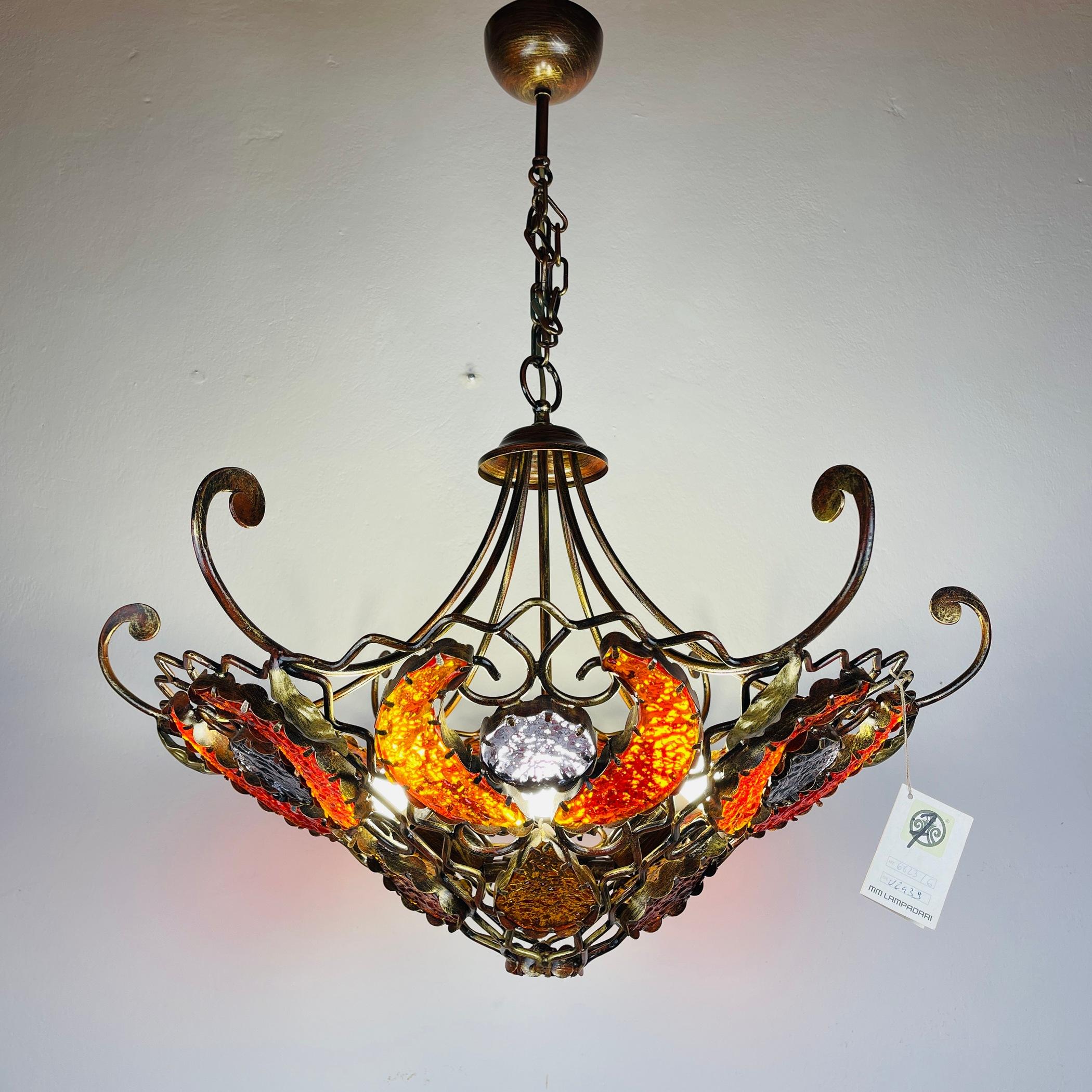 Introduce an exquisite blend of metal and Murano glass into your space with this chandelier by MM Lampadari, crafted in Italy during the 1990s, according to the catalog of MM Lampadari. Featuring wrought iron and vibrant Murano glass, this piece