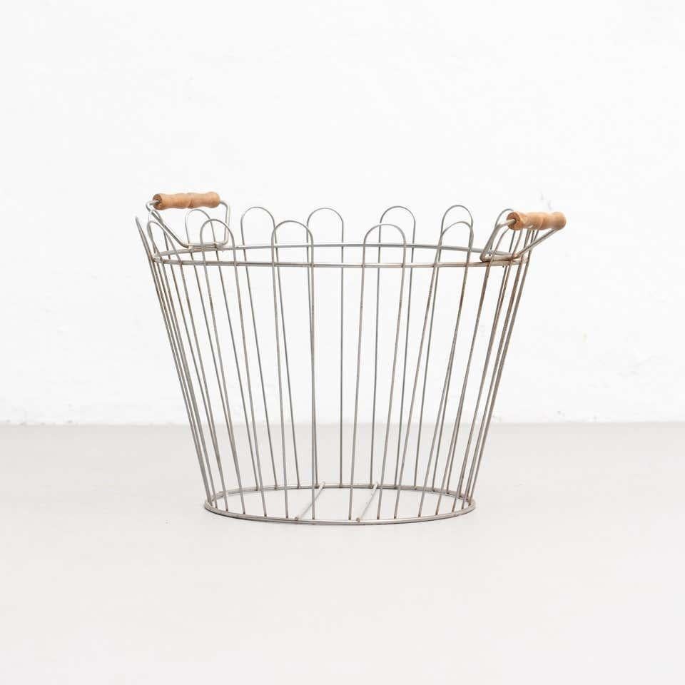 Panier en métal fait de fils soudés complétés par un anneau solide. Avec poignées en bois.  Fabricant inconnu, France,  Circa 1970    Matériaux :  Métal  Bois    En état d'origine, avec de légères usures dues à l'âge et à l'utilisation, préservant