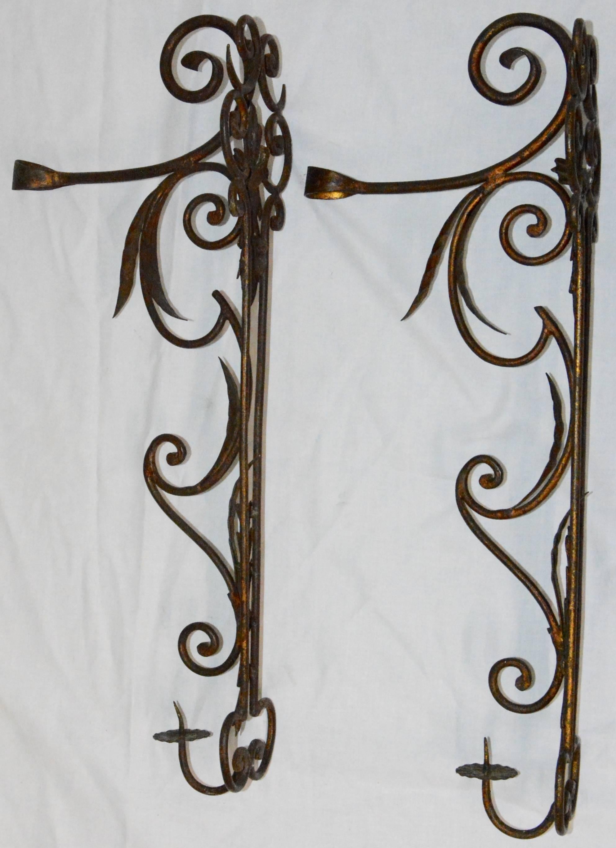 Featured is a unique pair of metal candleholder wall sconces. These are made of metal with a purposeful patina. They feature foliate details and scrolls, with a candleholder to the bottom. They are unmarked. The top has an arm that extends. Hangers