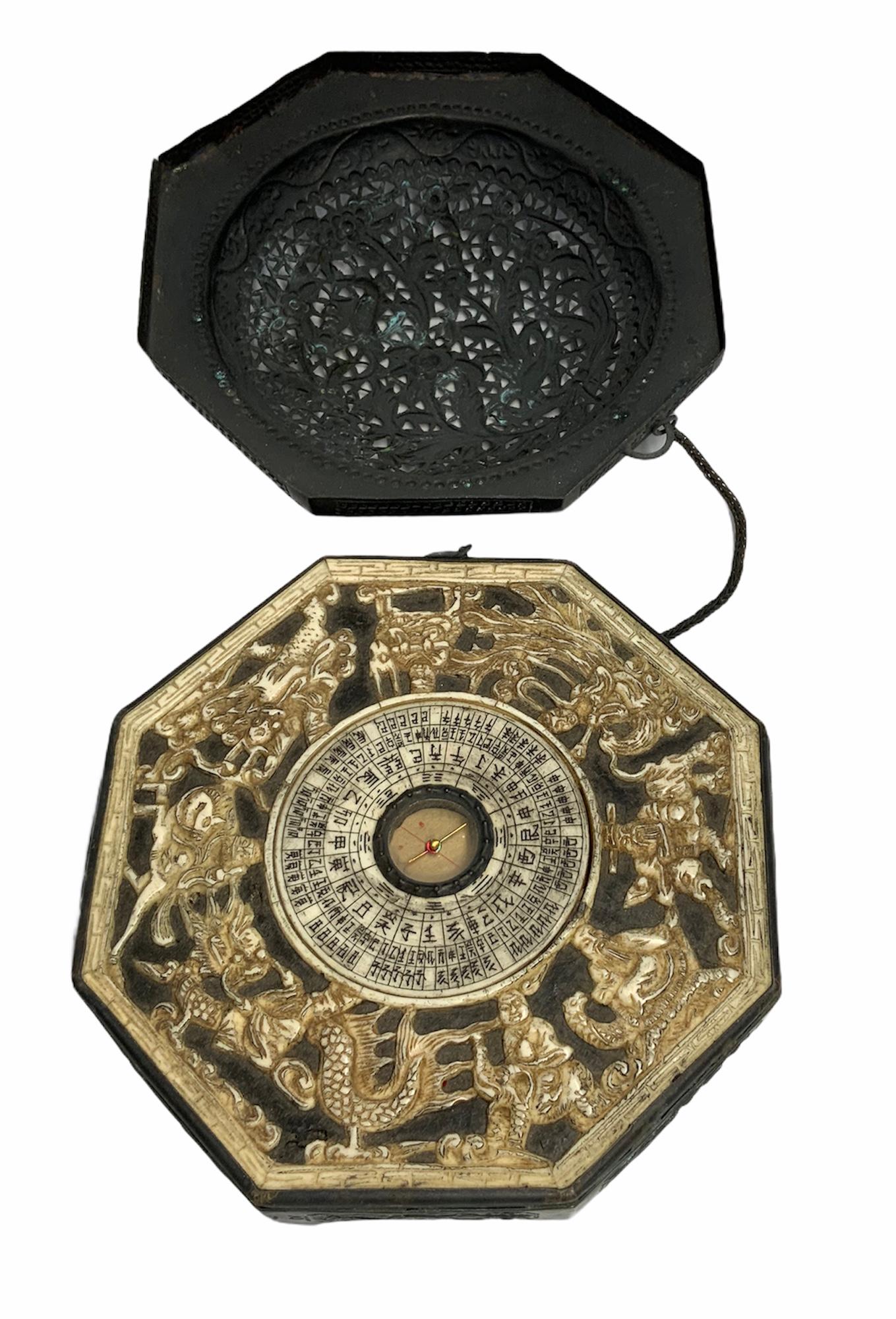 This is a reticulated metal octagonal dome box decorated in the front with flowers & foliage. In the back, there is some carving depicting a bird surrounded by scrolls and more foliage. Inside the box, it is found the Feng Shui compass surrounded by
