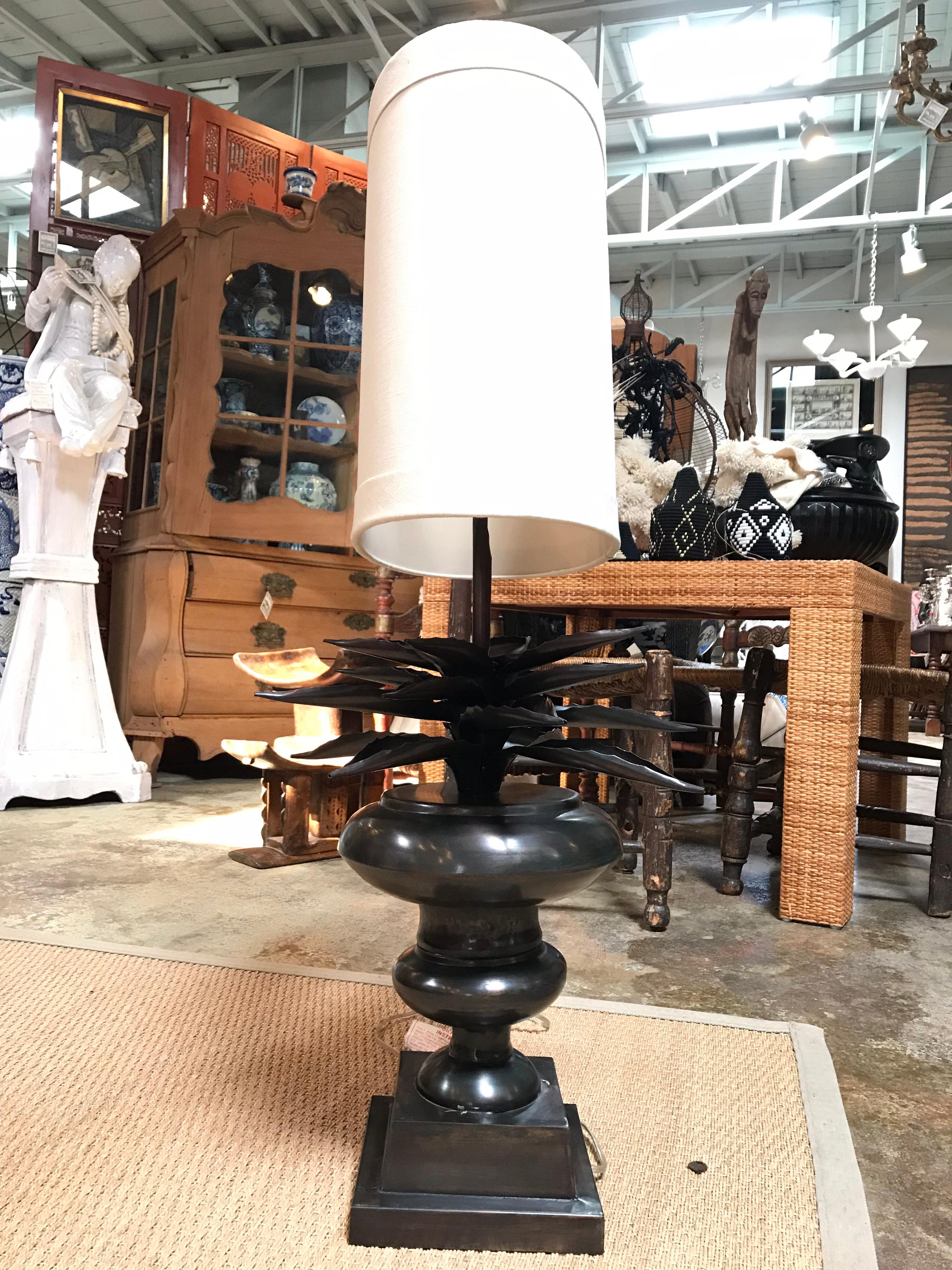 This hollow, metal cast lamp has decorative handmade layered Agave leaves fanning out around the lamp in a radial pattern. They are perched atop the lamp body and base. This item comes with a harp, an oblong shade and a matching topper.