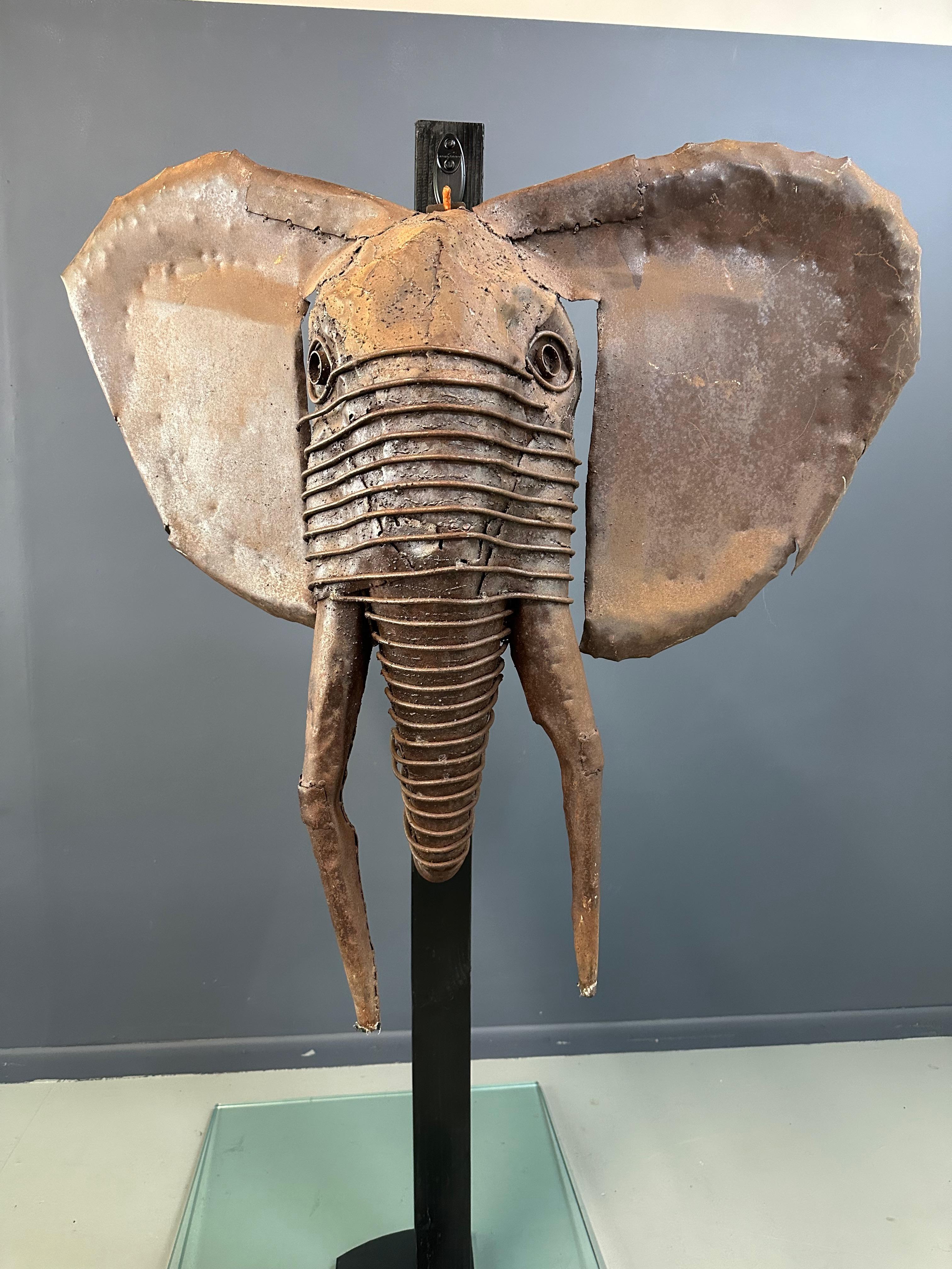 Questa scultura da parete a forma di testa di elefante in metallo è un'opera eccezionale del celebre scultore keniota Kioko Mwitiki (nato nel 1960), ampiamente considerato come un pioniere della scultura africana contemporanea in metallo. Mwitiki è