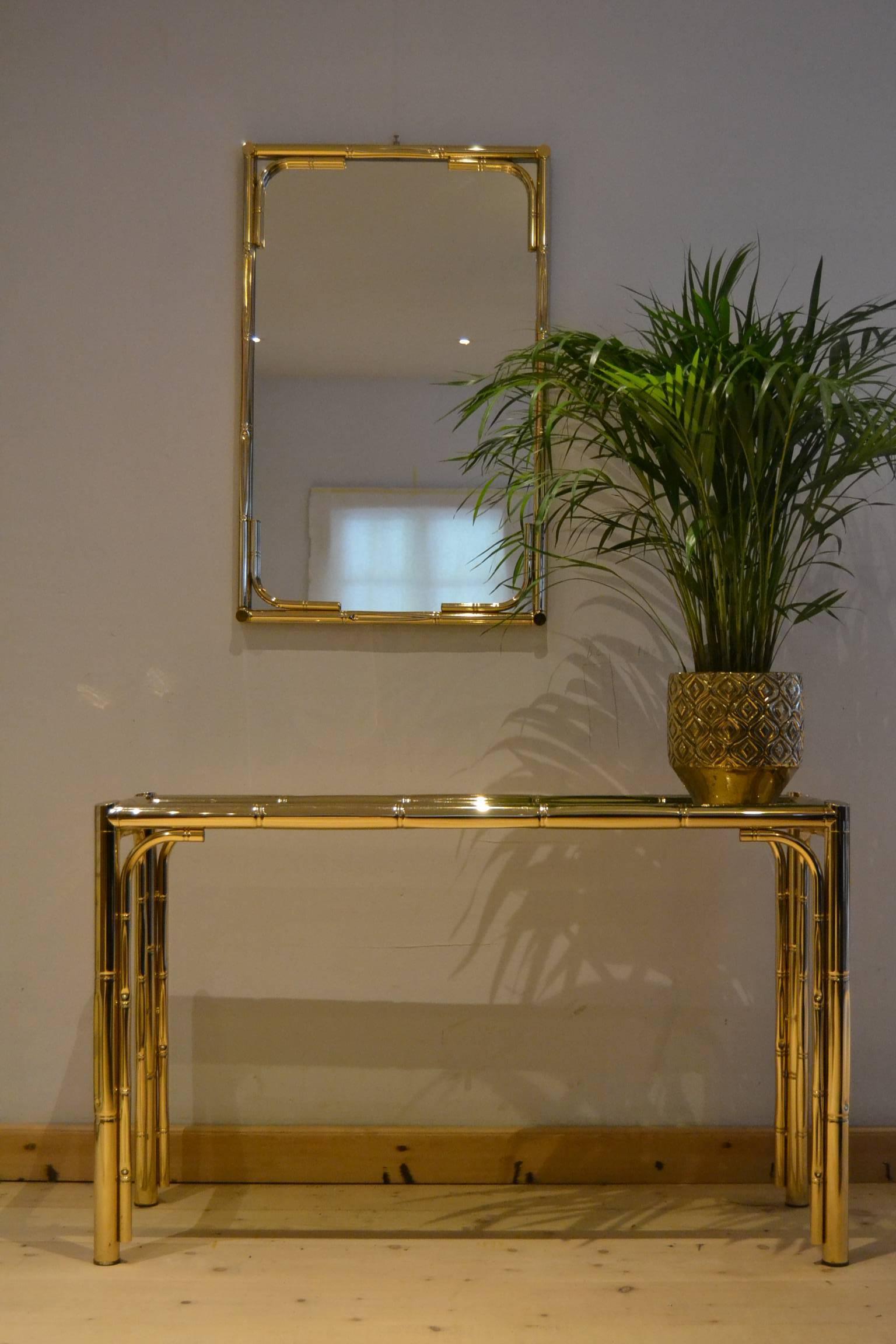 Elegant set of metal faux bamboo console table and mirror,
made in Italy in the 1970s.
The metal has a gold color, what makes this set very stylish.
The table, side table has a smoked glass top.  

This elegant set can be used to place in an