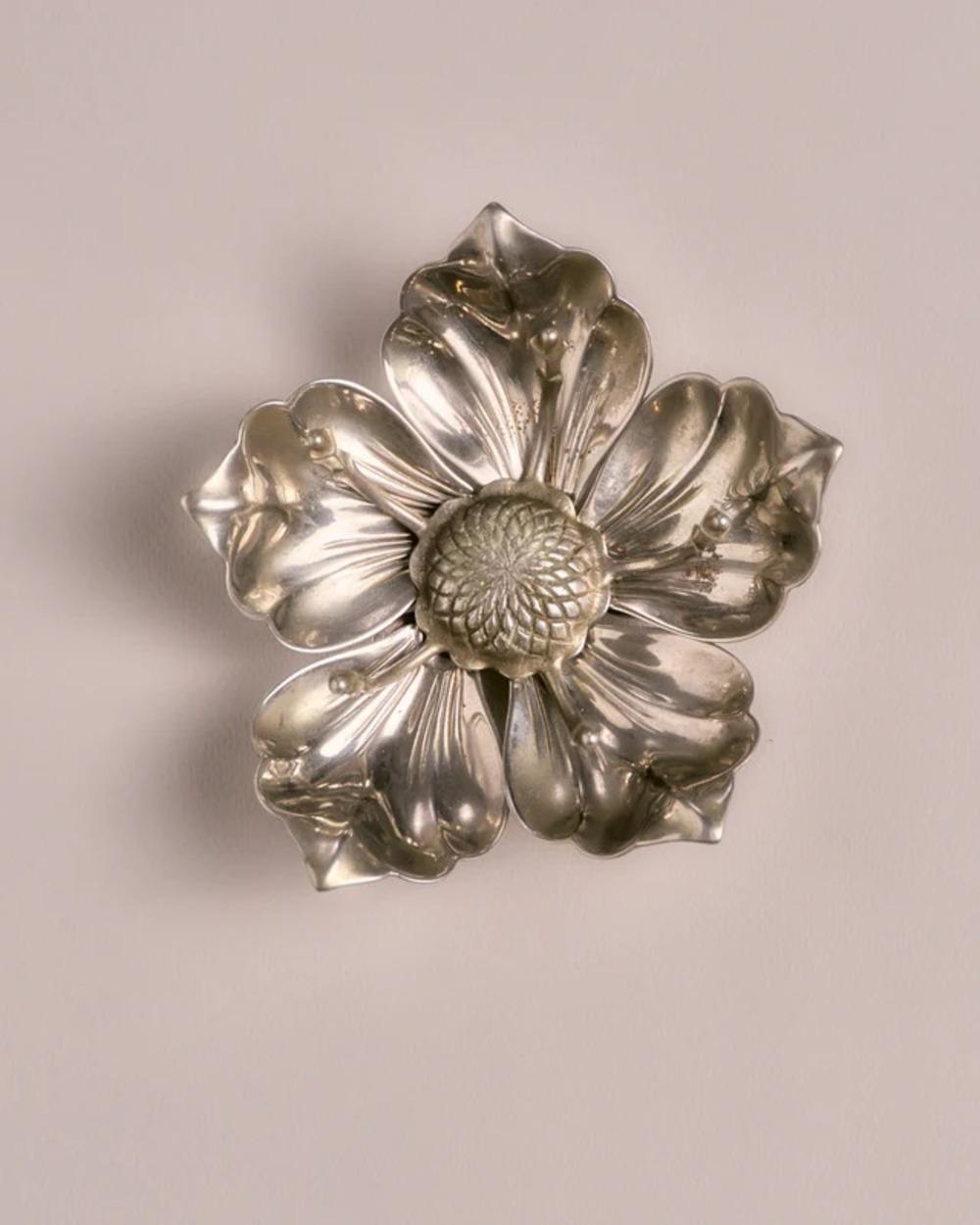 Satz von fünf einzelnen Aschenbechern aus Metall, die auf einem passenden zentralen Ständer ausgestellt sind. Jeder Aschenbecher hat die Form eines Blütenblattes. 