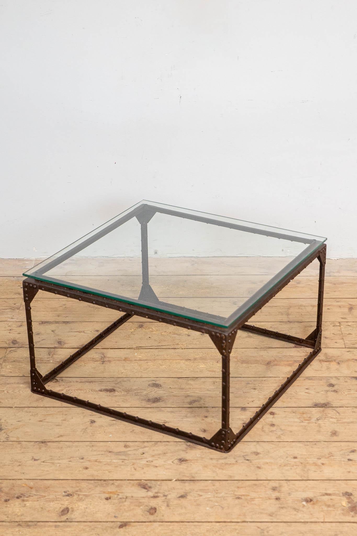 Cette table basse unique était autrefois une caisse industrielle provenant des Pays-Bas. Son cadre métallique robuste et riveté porte les marques du temps, mettant en valeur la beauté brute de son passé industriel. Le plateau en verre nouvellement