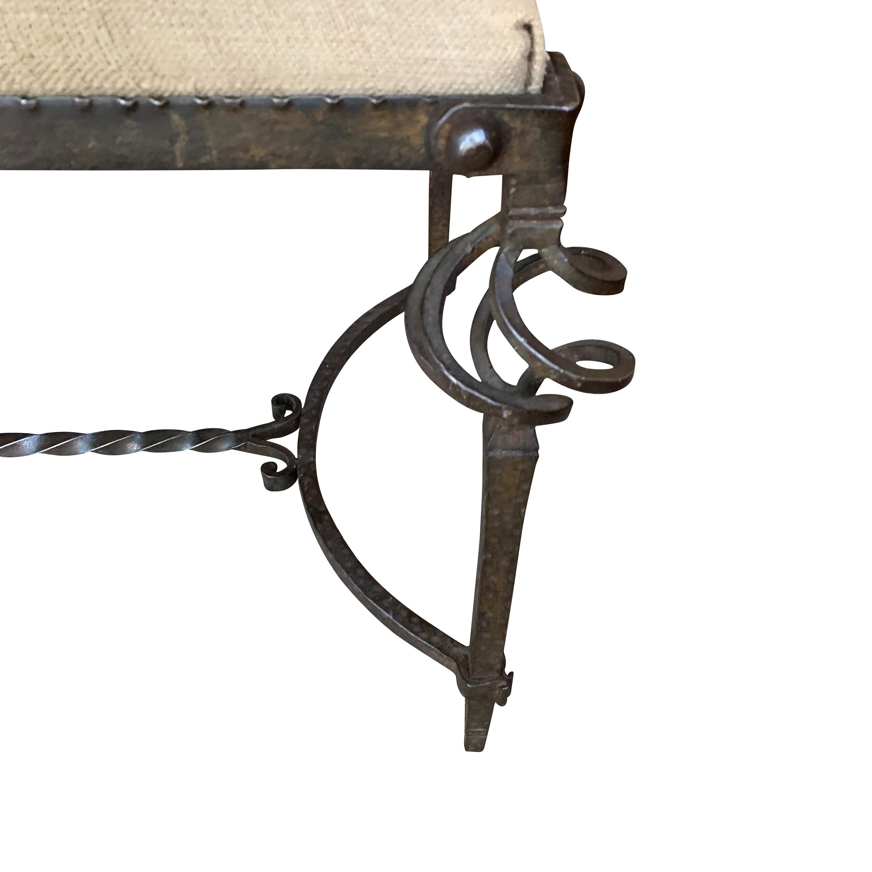 The frame of this 1940s Spanish upholstered bench is metal having a spiral decorative design on each leg. The stretcher is also spiraled with a decorative design at each end.
The bench has been newly reupholstered in hand spun Belgian vintage