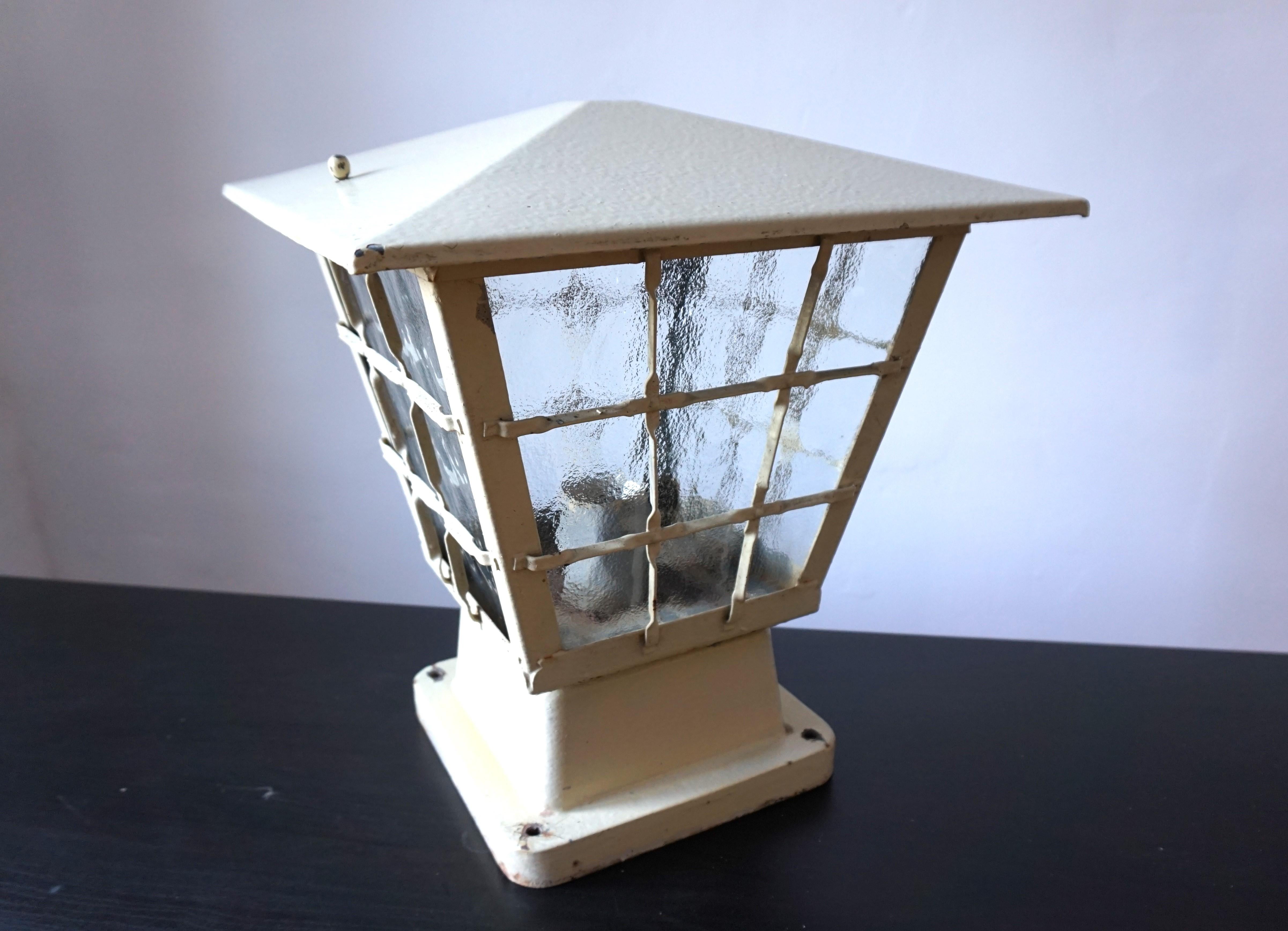A very massive garden lamp in a traditional 60s design. The lamp is made of metal and coated with an ivory-colored paint, presumably the original paint. The lid is designed in the form of a tent roof and can be removed using two screws. The glass