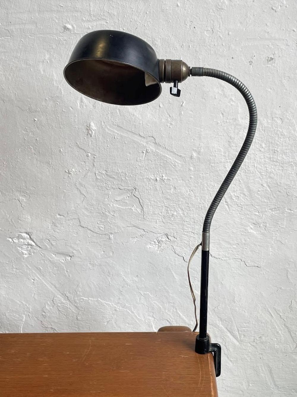 Esta lámpara de escritorio de estilo industrial presenta los elementos de diseño característicos de la iluminación de trabajo de mediados del siglo XX, con su pantalla en forma de cúpula, su cuello de cisne flexible y su base robusta. Ejemplifica el