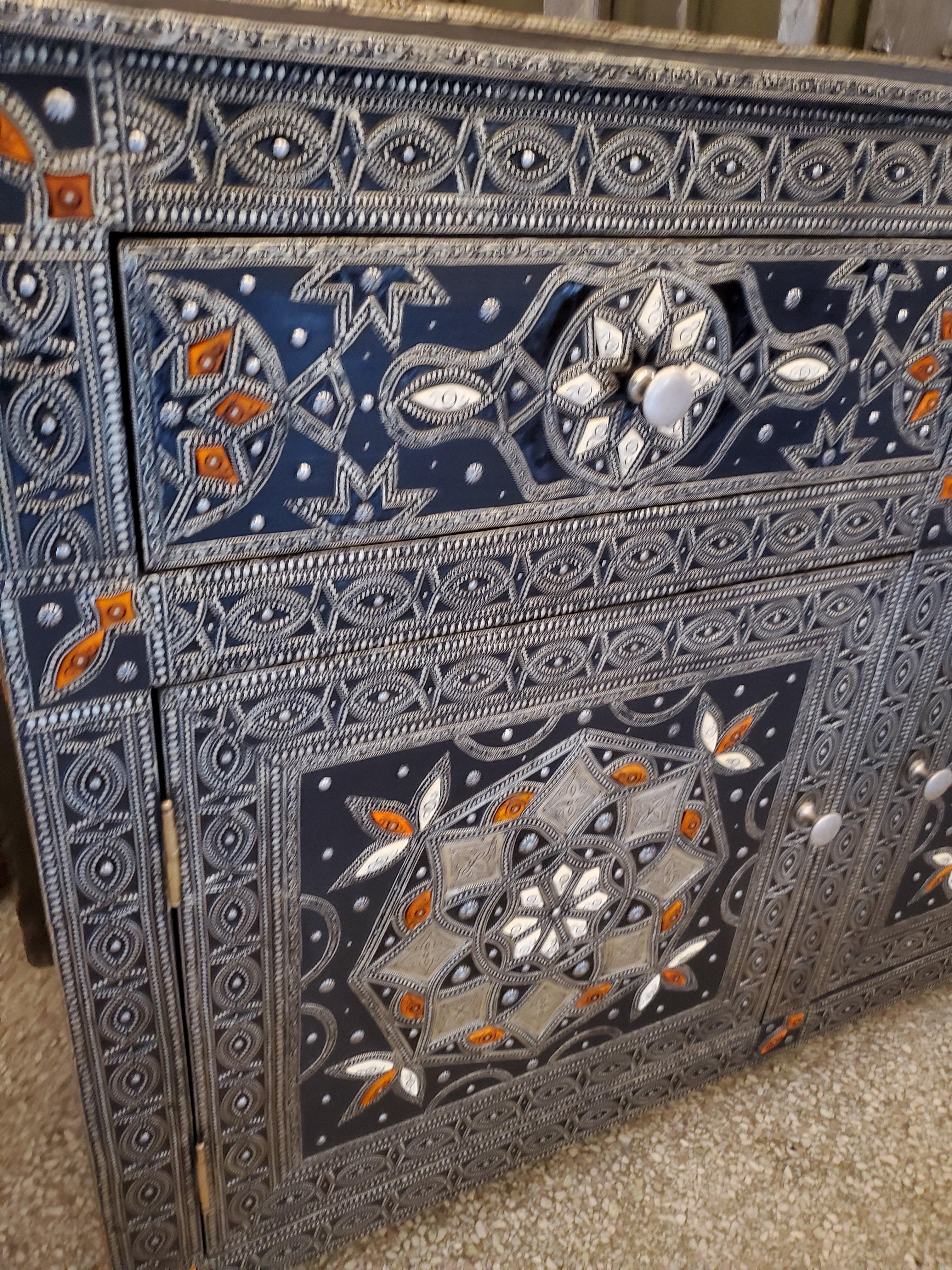Aged all metal inlaid handmade Moroccan wooden cabinet measuring approximately 34” in height, 49” in width, and 16.5” in depth, and featuring 2 easy access doors and two easy to open drawers above. Plenty of storage. Lots of details throughout. Can