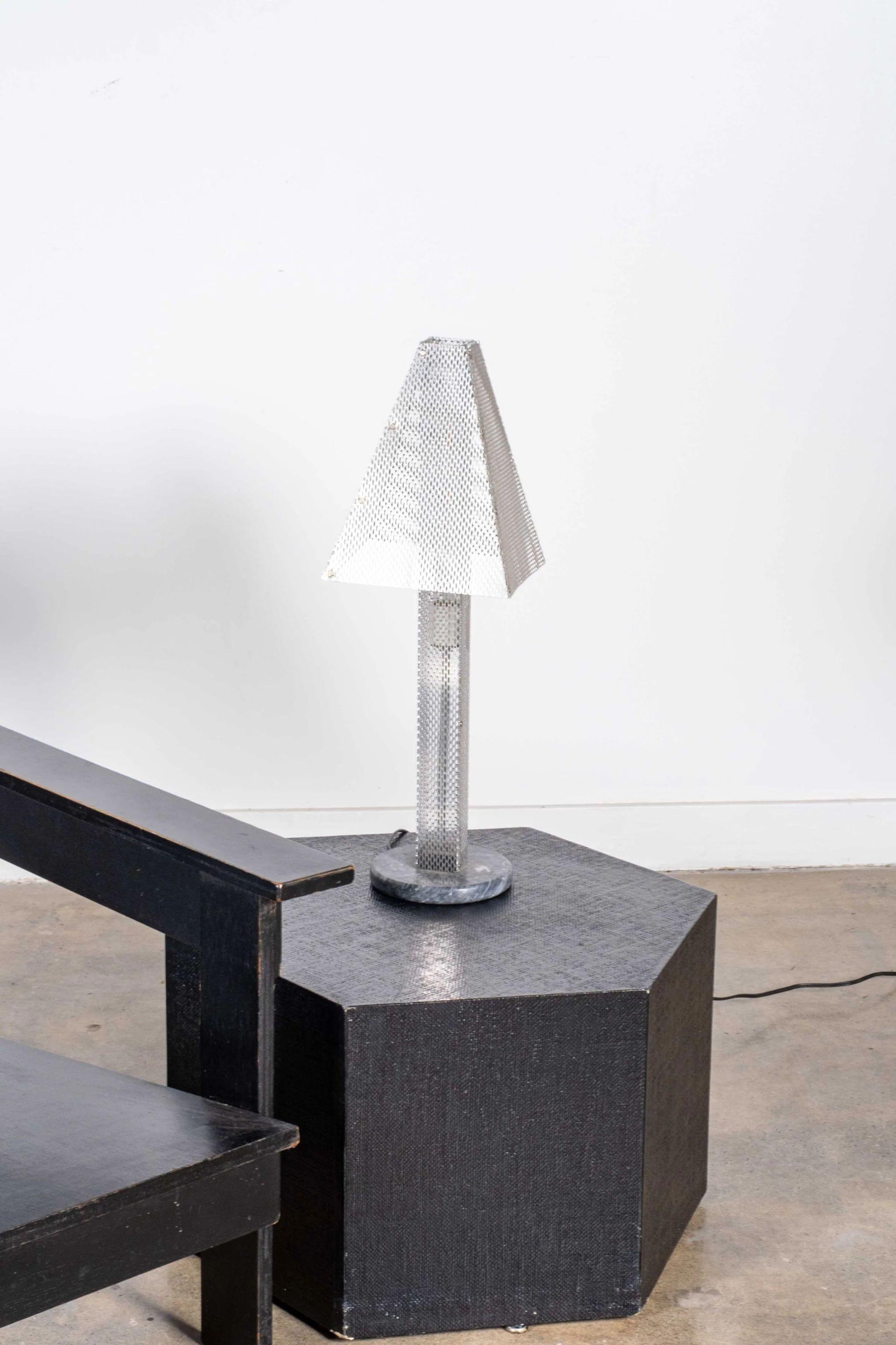 Perforated metal planes make this lamp a high tech addition to any tabletop. Its reflective surfaces bounce light around even when the bulb is off. A black marble base brings the shiny shenanigans down to earth. A piece destined to play a starring