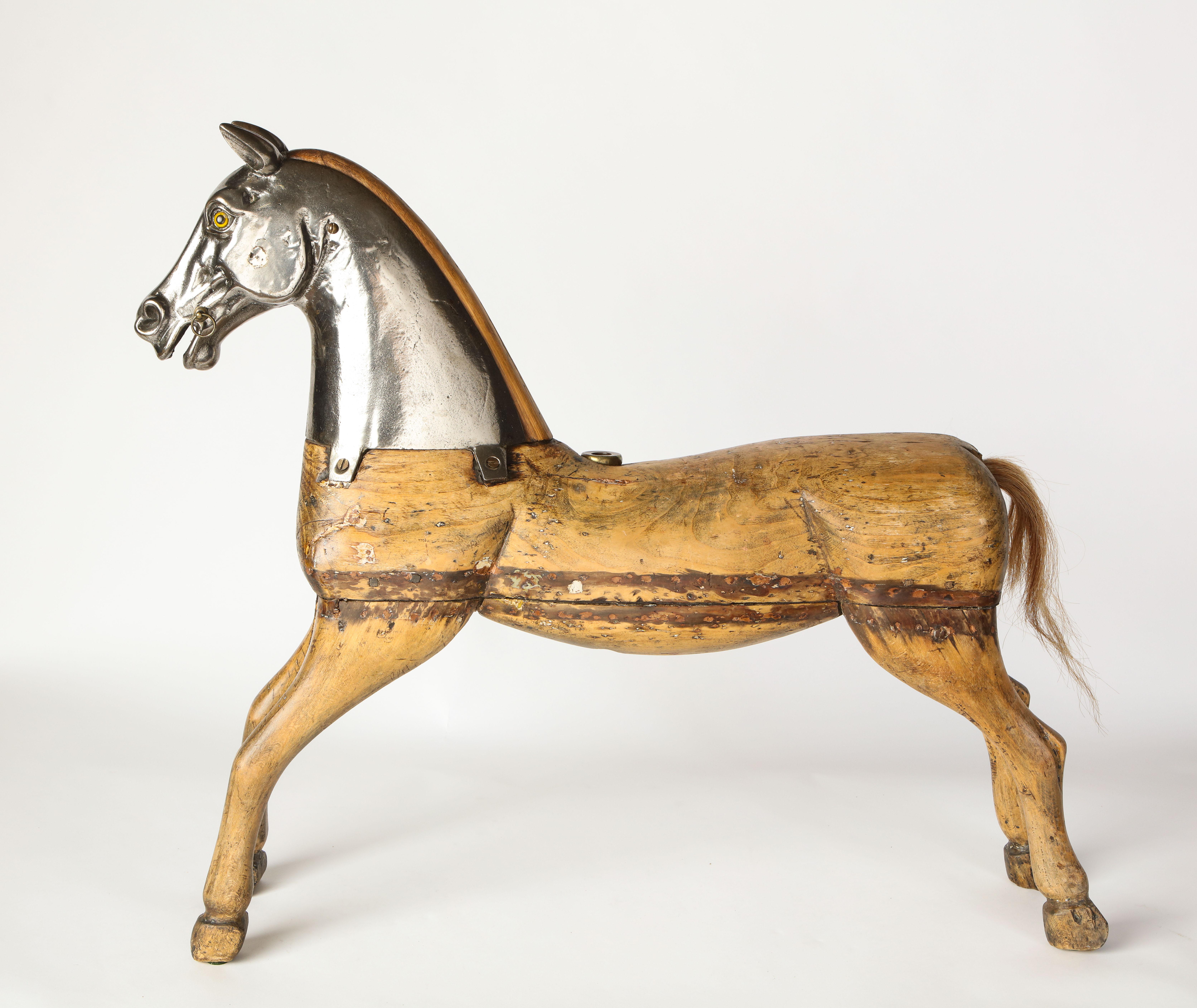 A metal-mounted pine carousel horse from the early 20th century. Modeled as a leaping horse, with inset glass eyes. Its top portion, modeled in metal, beautifully contrasts the bottom portion, modeled in pine, to create a statement decorative