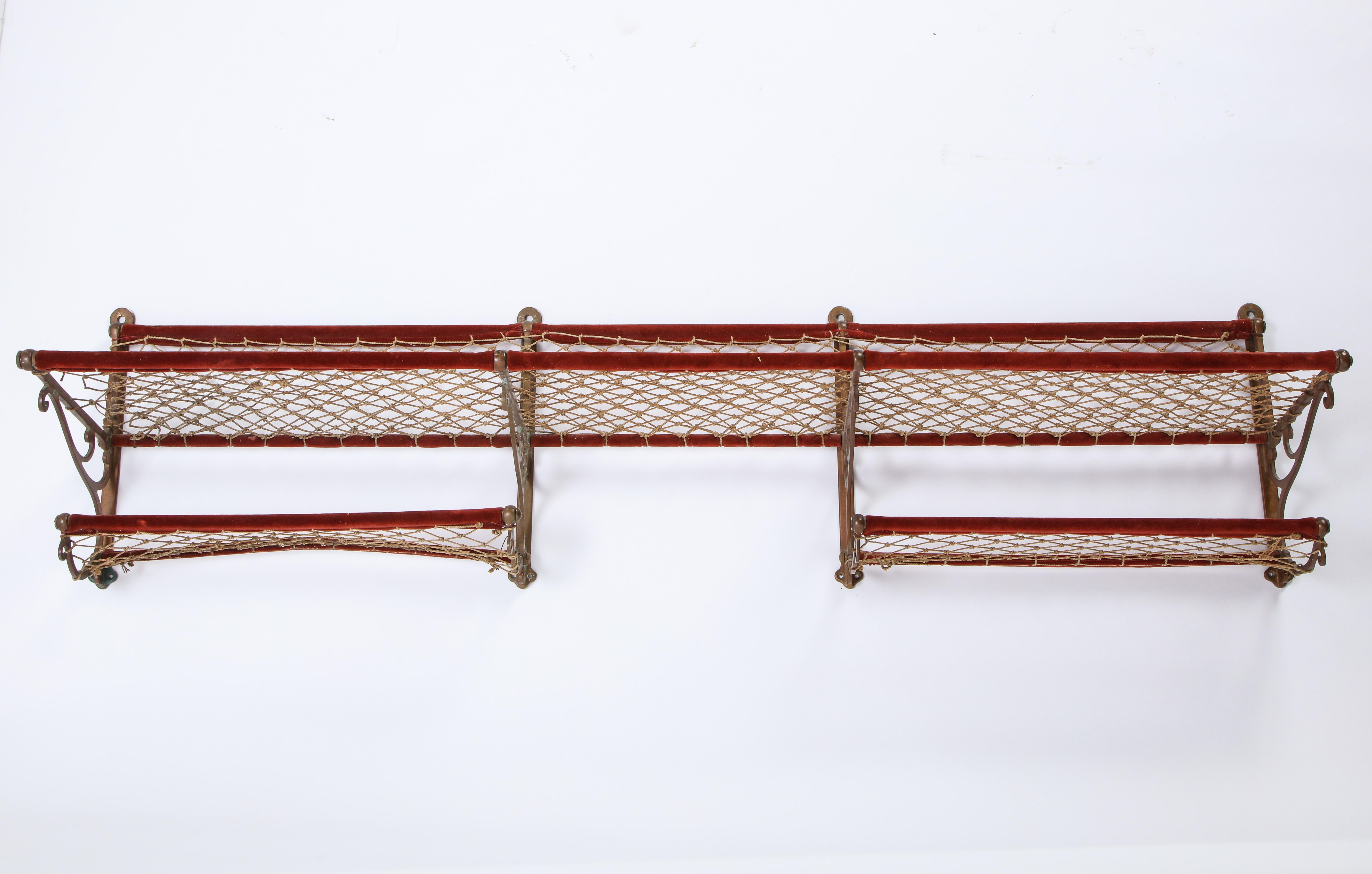 This large metal luggage rack with red plush trimming and netting probably dates to the early 20th century. Tracing its ties to a European train, this piece is both functional and decorative, adding a late Victorian flair to any room. Choose to add