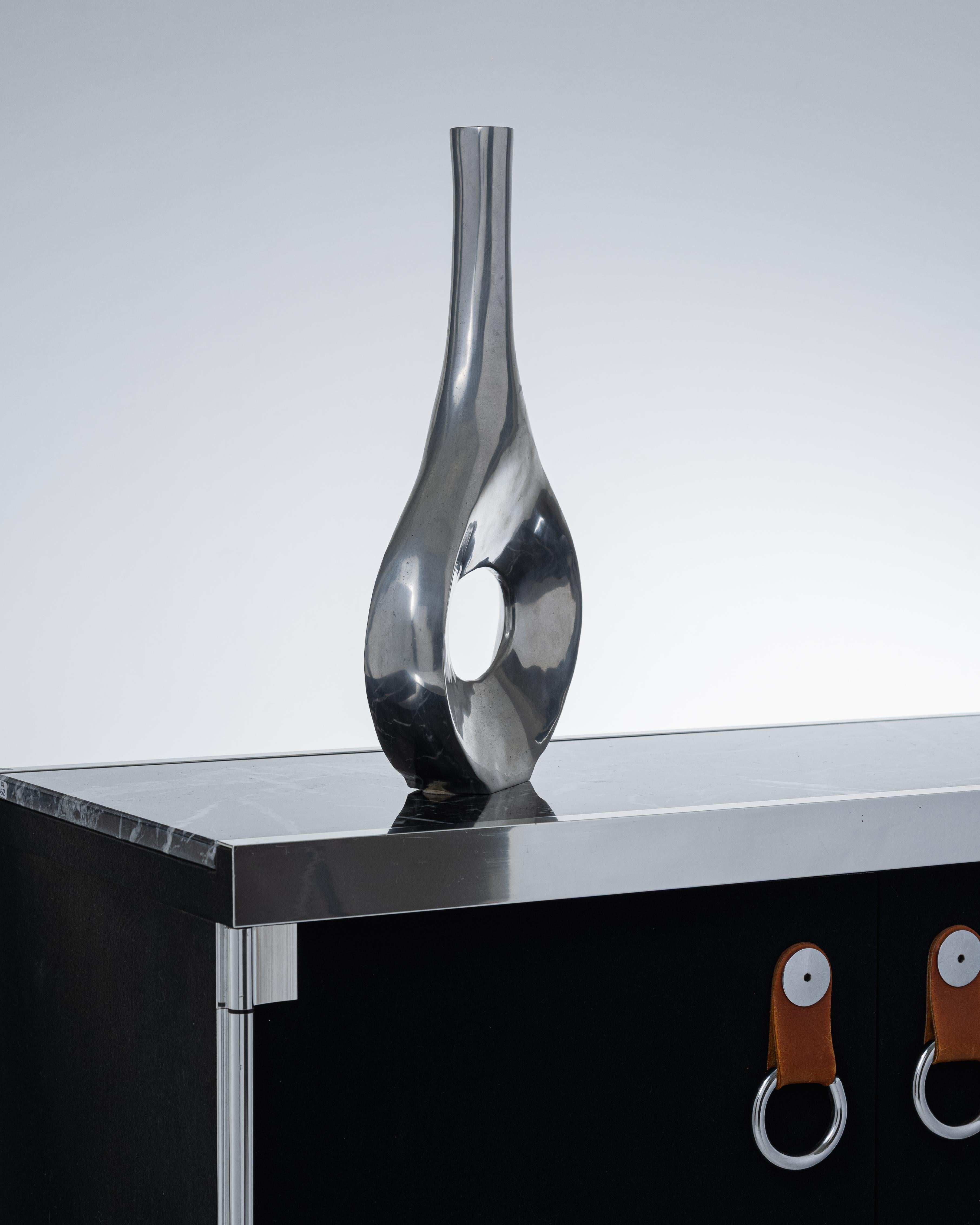 Polished aluminium single-flower vase, emblematic of 1980s design.
Its graphic silhouette is distinguished by an openwork base with a large central void, extended by a slender neck. A unique piece, both decorative and sculptural, in keeping with