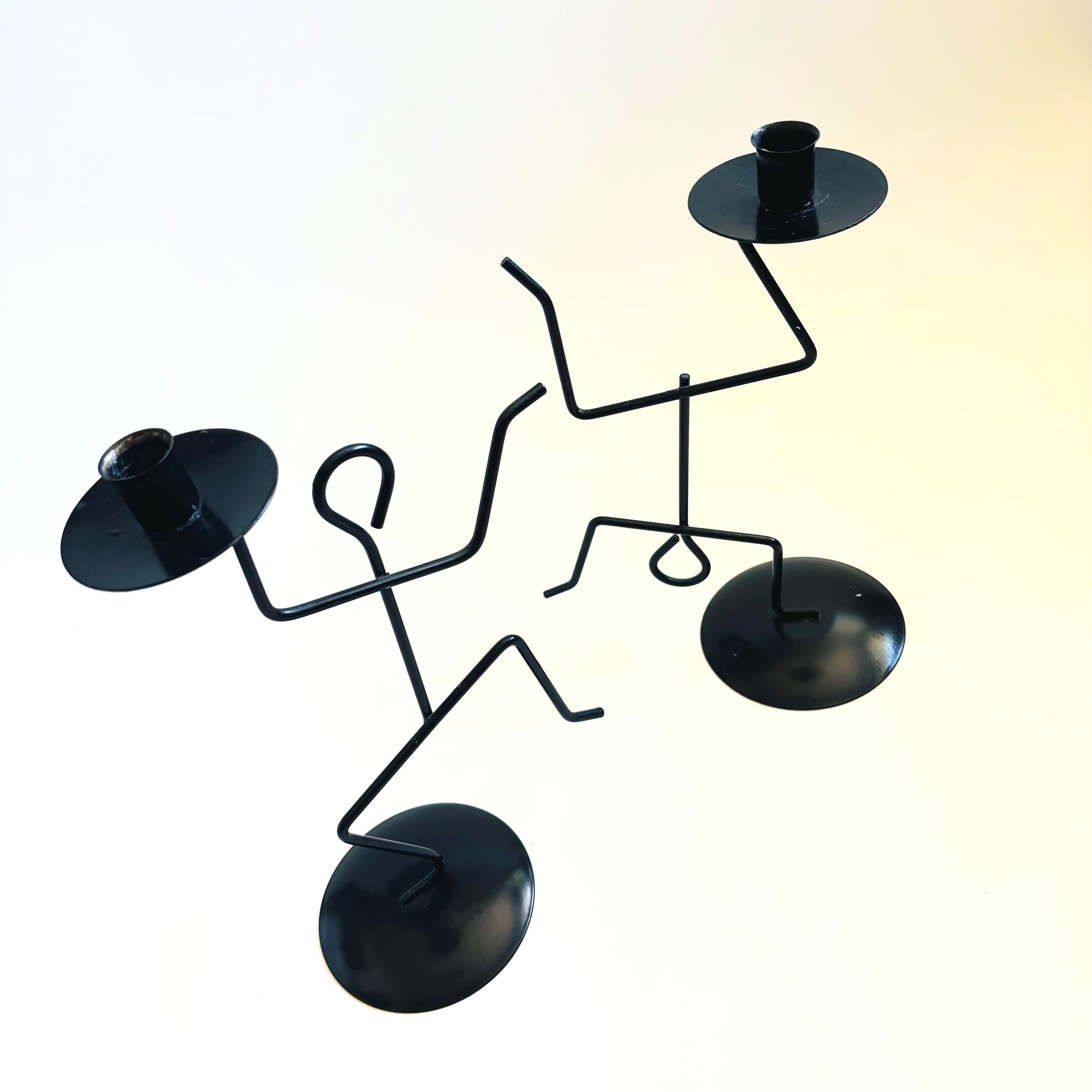 A pair of vintage black metal candles holders, each in the shape of a stick person.

