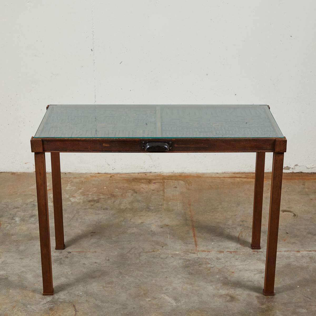 Industrial glass top table with graphic lettered top. This unique table began its life as a typeface tray in late 19th-century France. Having since been mounted on rectangular iron legs and given a glass top, the table's design reflects its